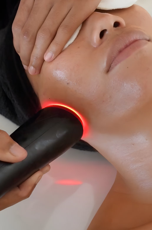 A person receiving a facial treatment with a handheld device emitting red light on their cheek.