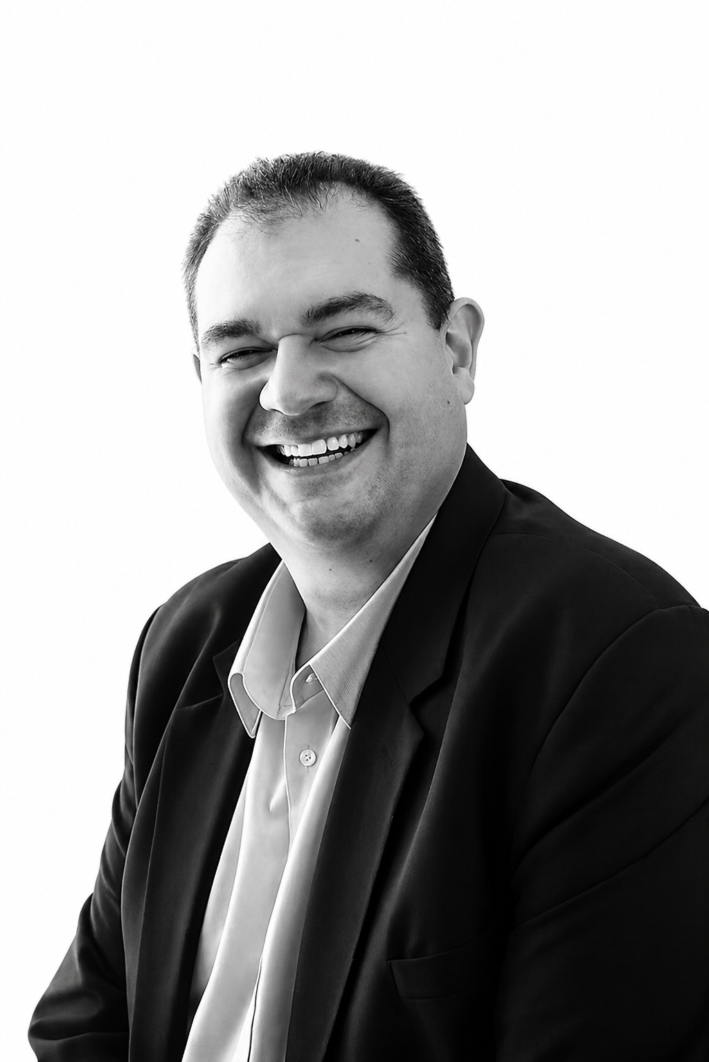 A black and white portrait of Michael Gershkov wearing a suit jacket and a collared shirt, having a little laugh.