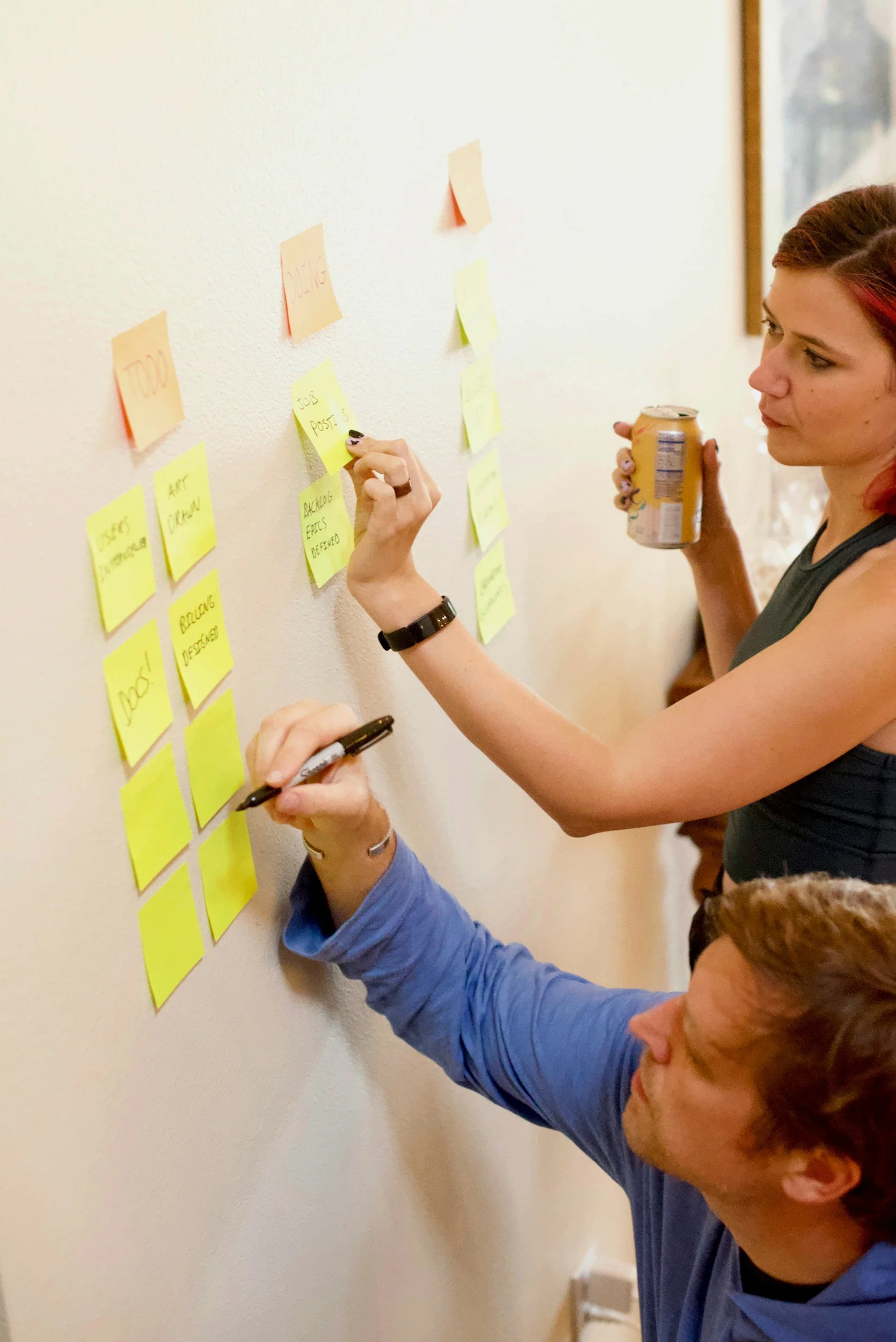 People writing and arranging colorful sticky notes on a white wall during a brainstorming or planning session.