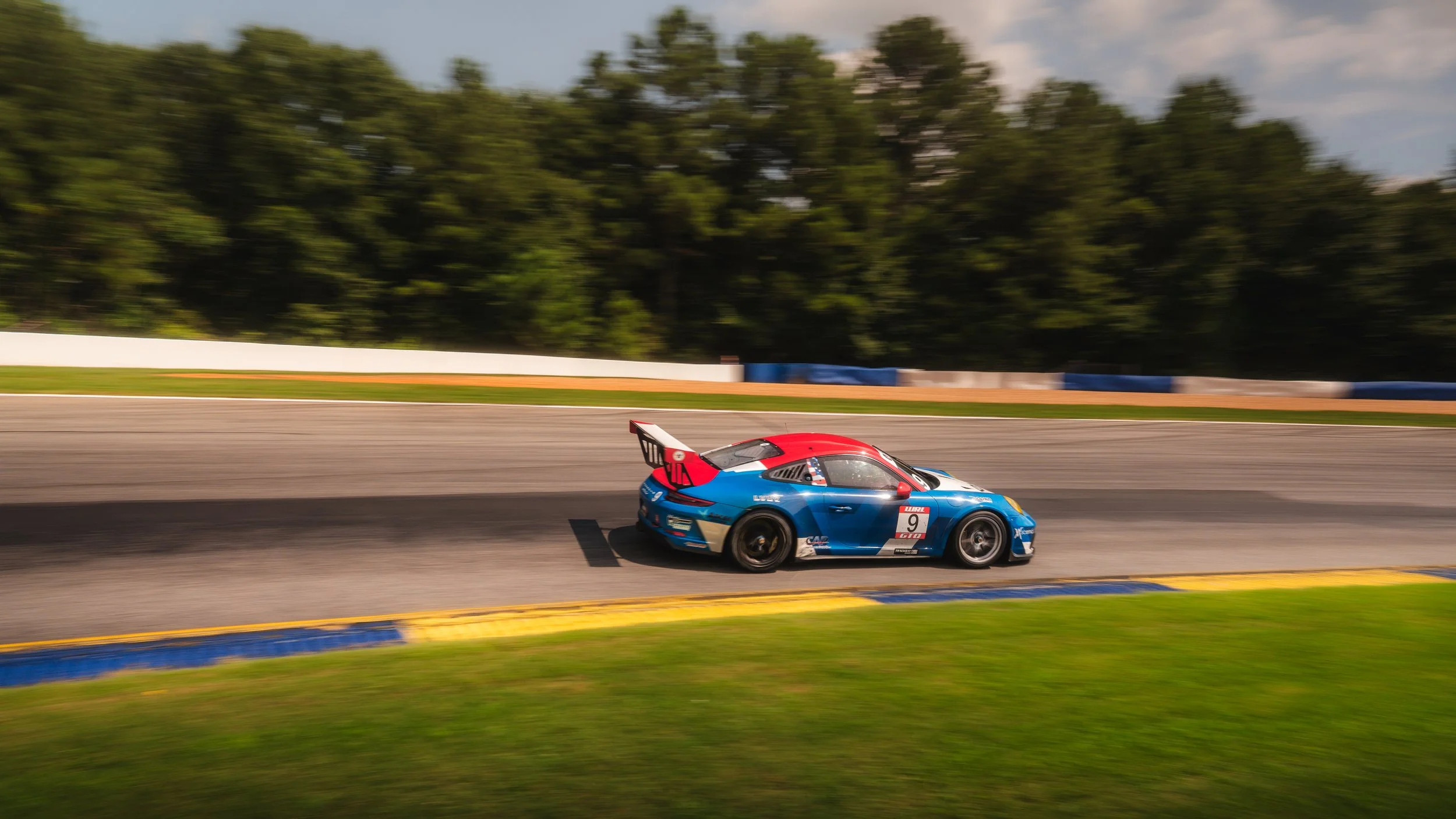 A Porsche GT3 race car on a racetrack with trees and a blue sky in the background. Road Atlanta