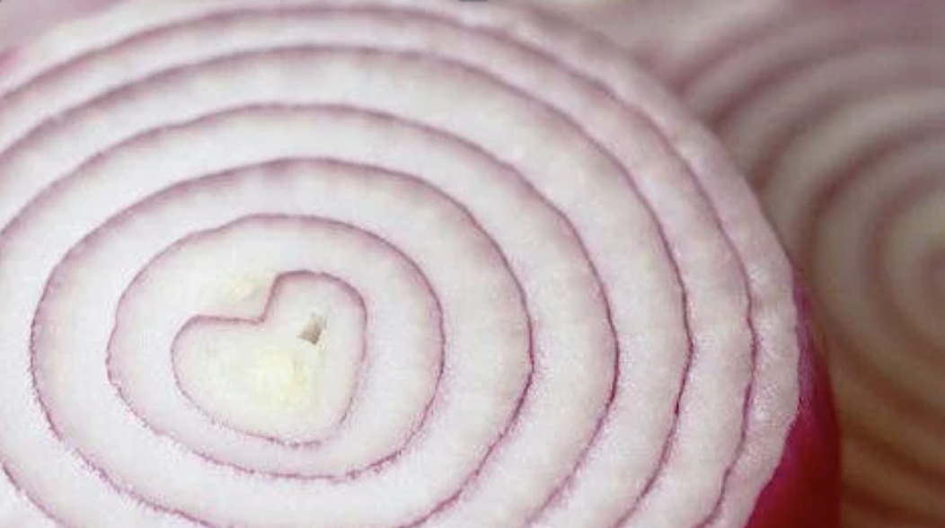 Close-up of a sliced red onion with concentric rings, with a heart-shaped pattern in the center.
