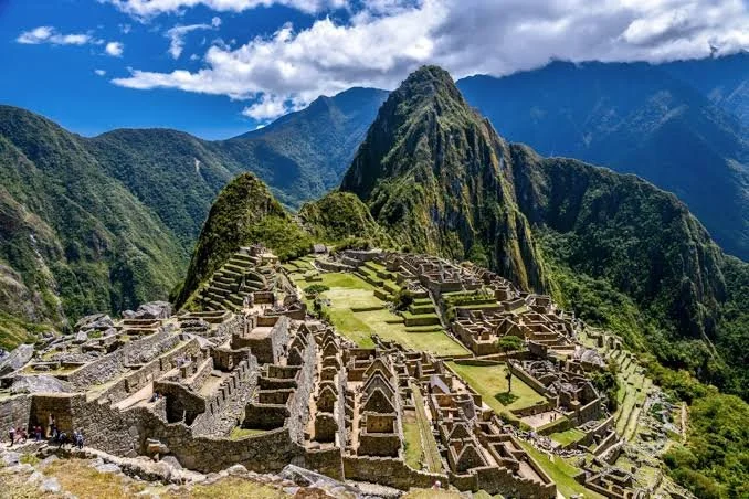View of Machu Picchu ancient Inca citadel surrounded by green mountains under a partly cloudy sky.