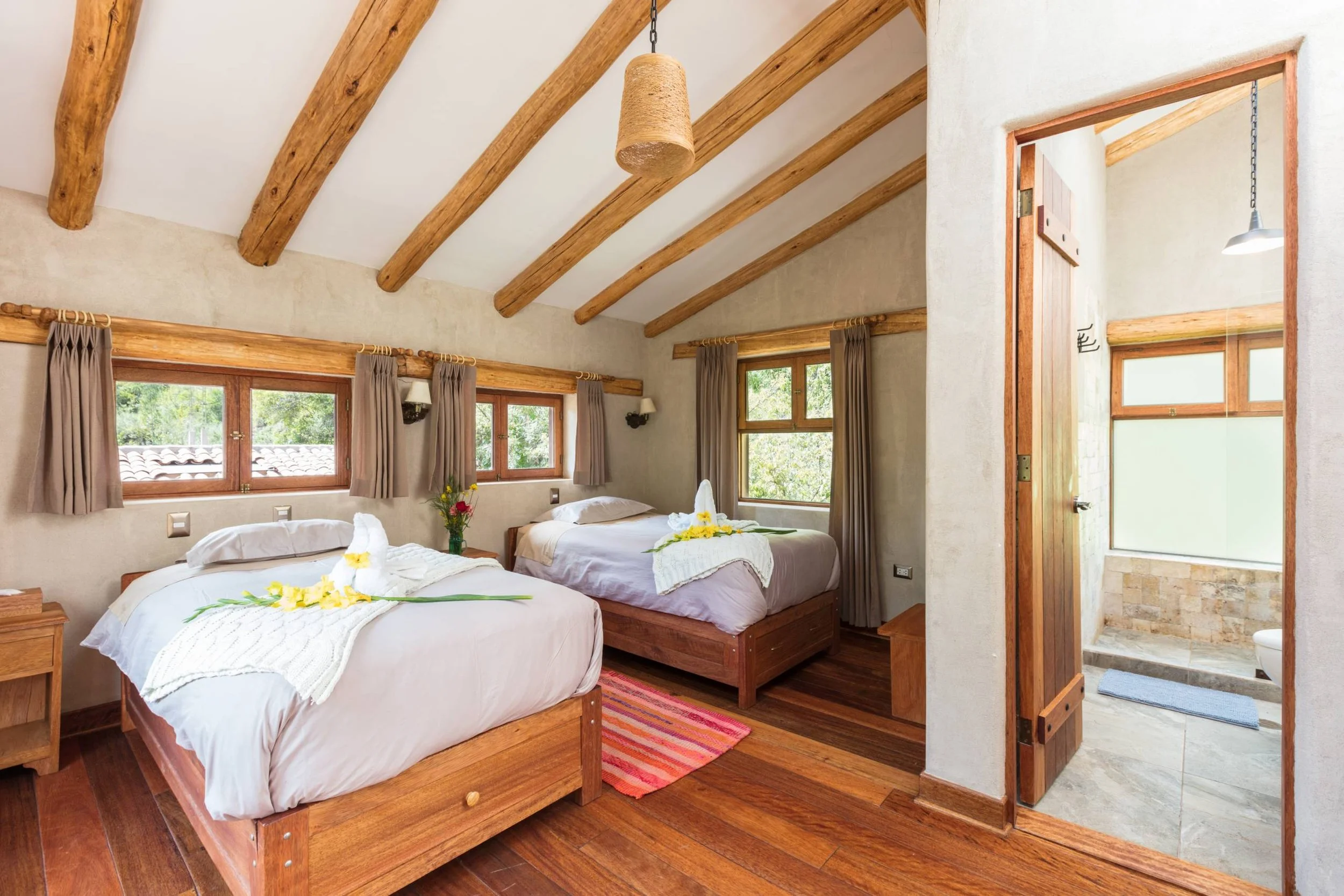 A cozy bedroom with two beds, wooden frames, and floral decorations, adjacent to a bathroom with tiled walls and a shower area.