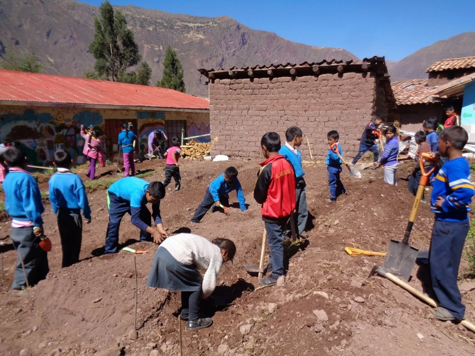 Children working together outdoors, planting and cultivating soil in a rural area with traditional buildings and mountains in the background