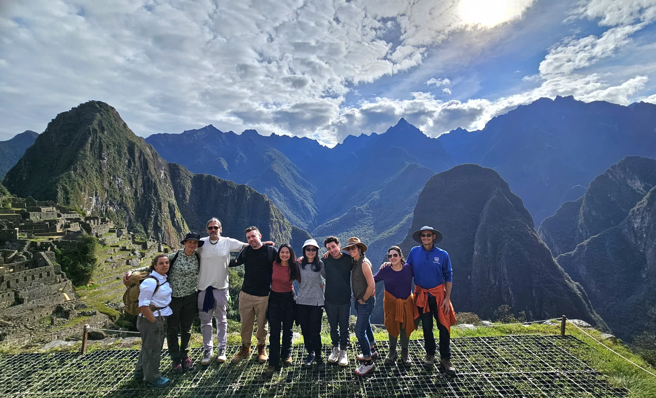 Group of ten tourists posing in Machu Picchu with mountains and ruins in the background.