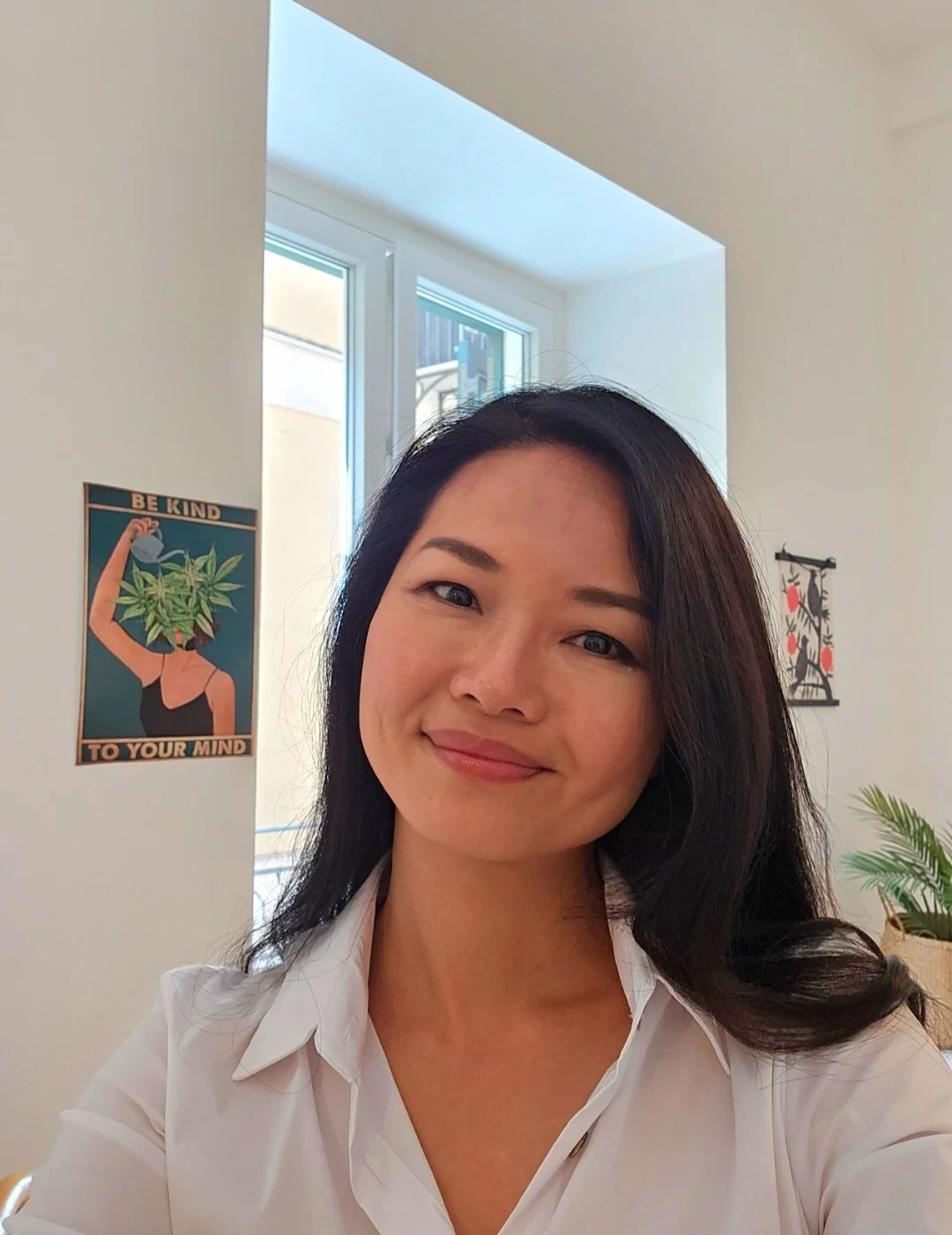 A woman taking a selfie in a bright room with artwork on the walls and a plant nearby.