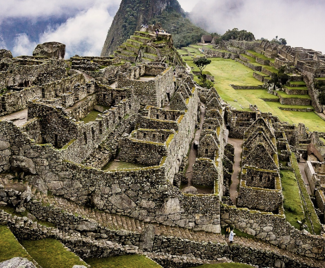 Ancient Incan ruins at Machu Picchu with stone terraces and buildings on a mountainside, surrounded by lush green landscape and cloudy sky.