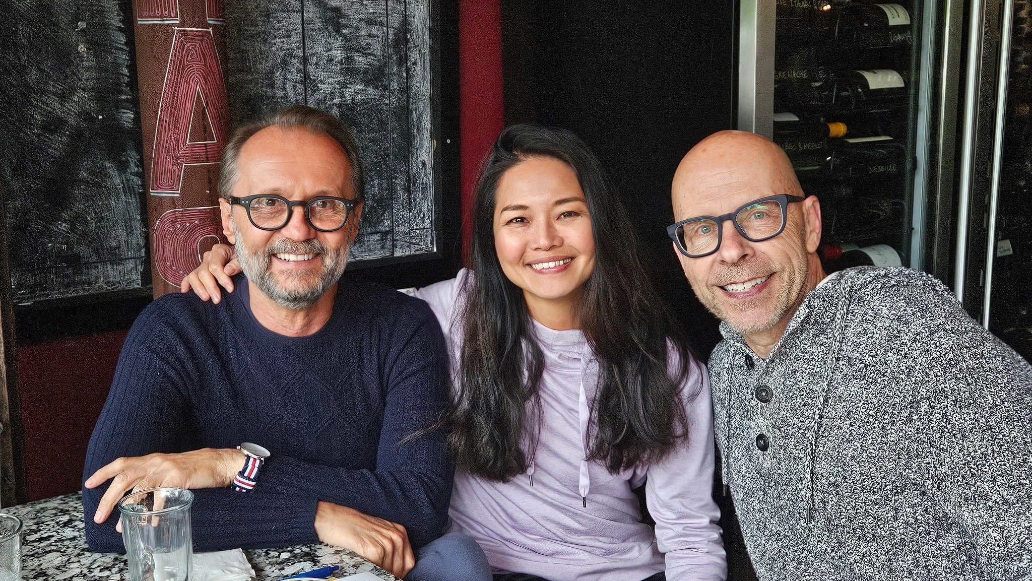 Three people sitting at a table in a restaurant, smiling at the camera.