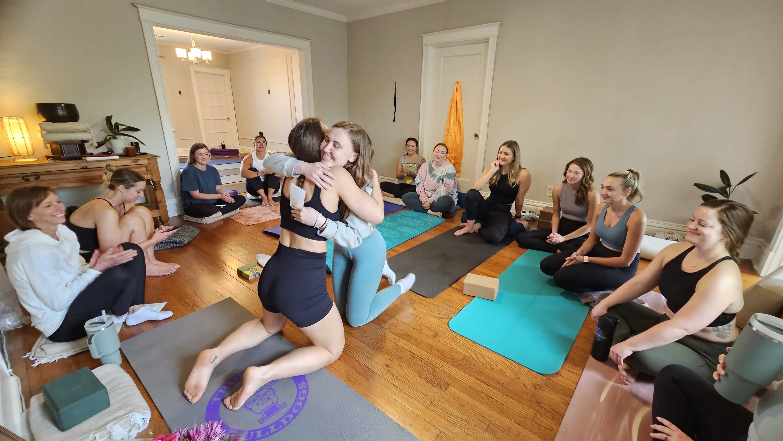 Women participating in a yoga or fitness class, with two women hugging in the center.
