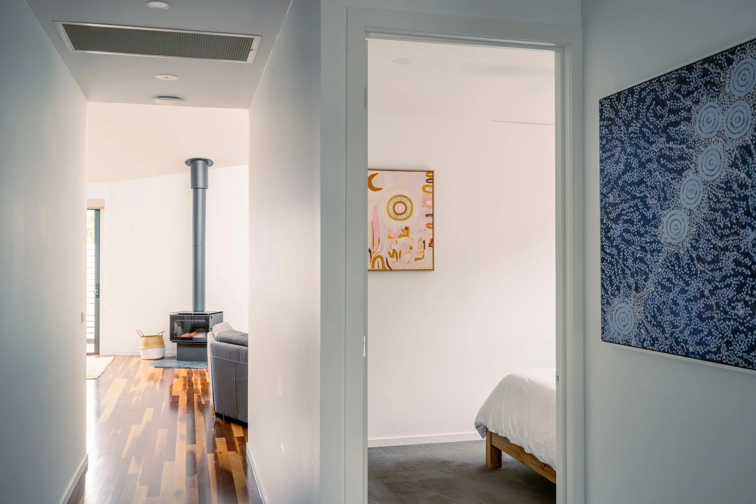 View of a hallway leading to a living room on the left and a bedroom on the right, both with white walls and contemporary decor.