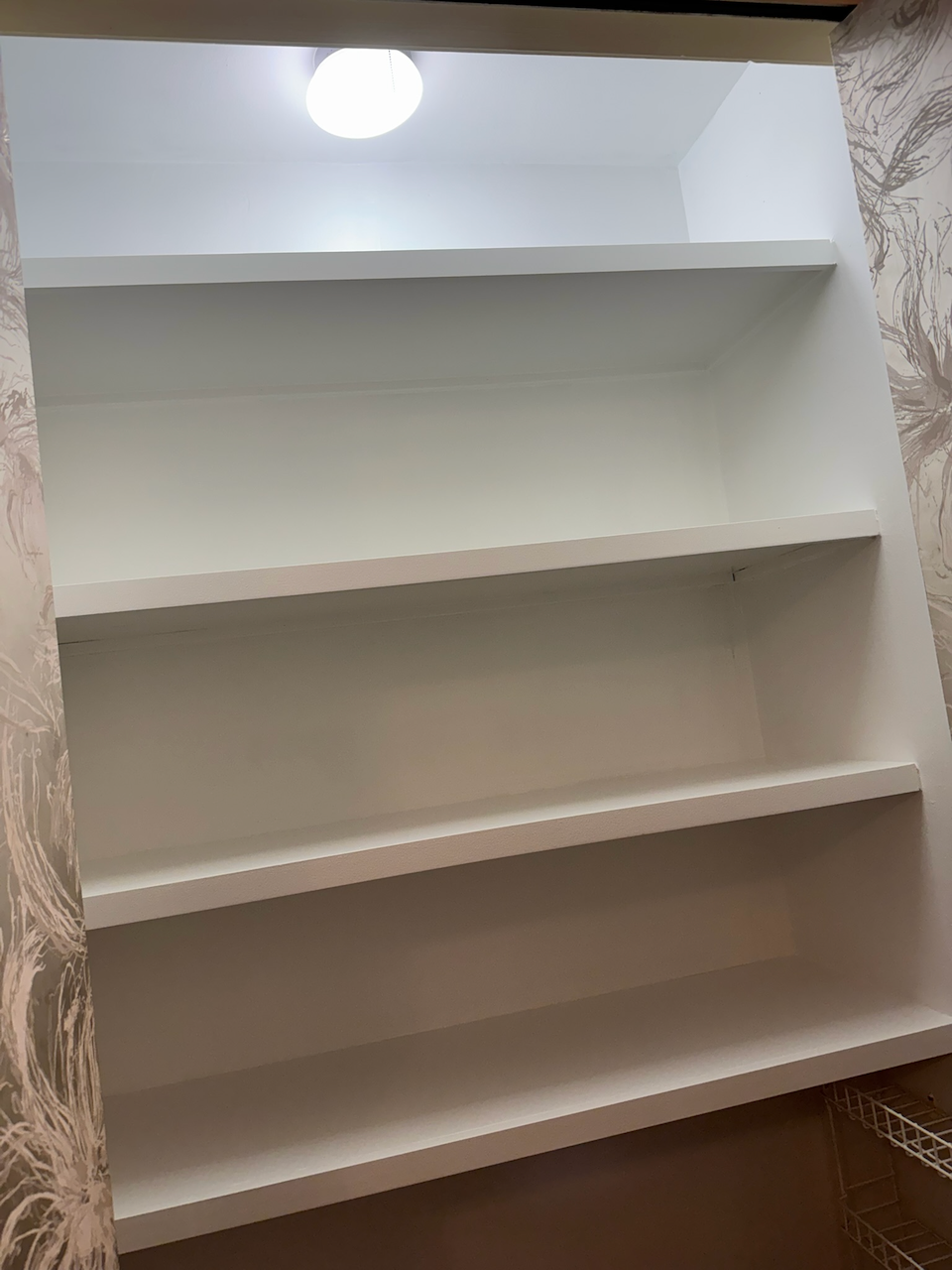 White built-in bookcase fitted into a wallpapered niche.