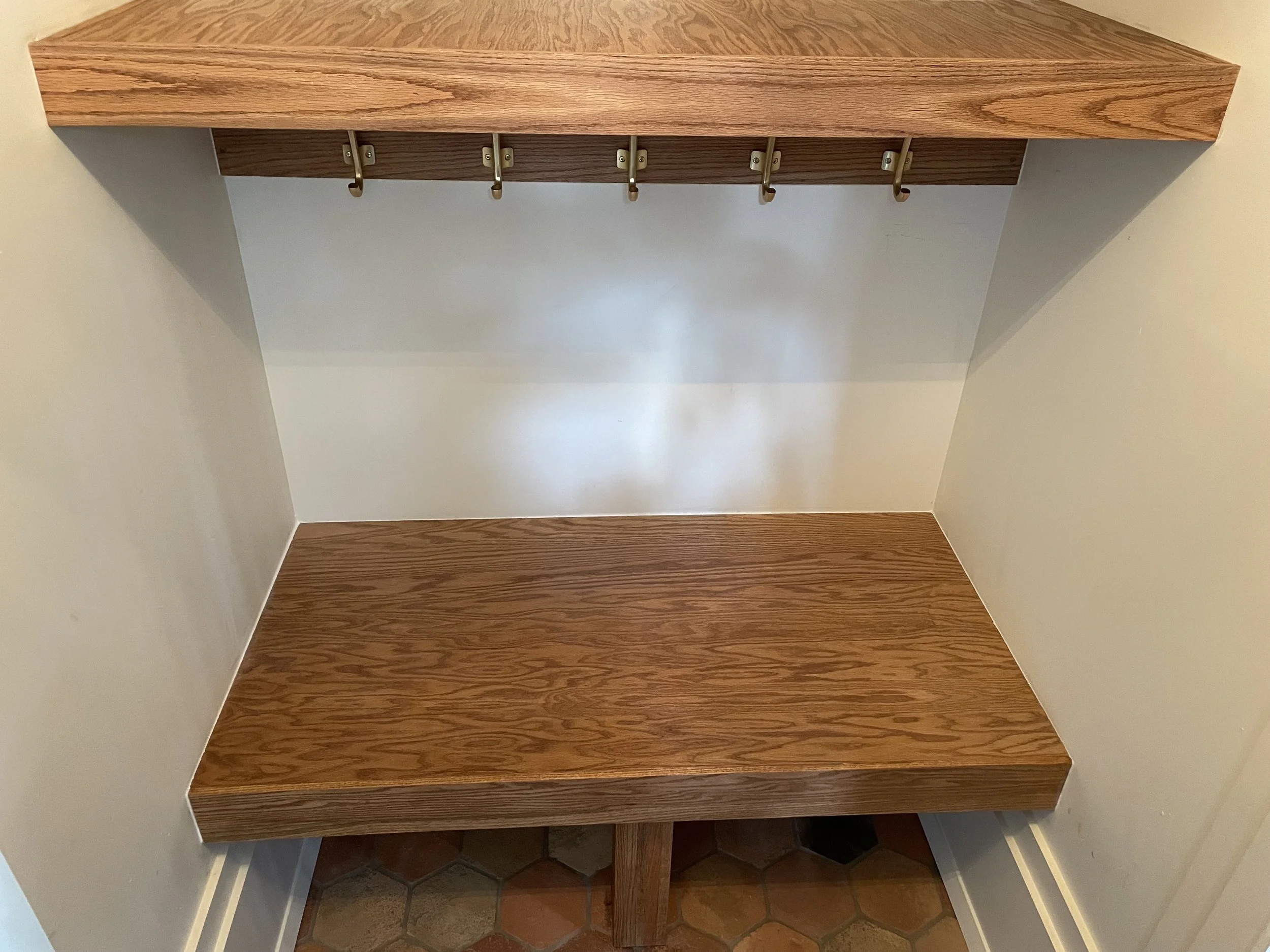 Custom oak bench and matching shelf fitted wall to wall in an entry nook.