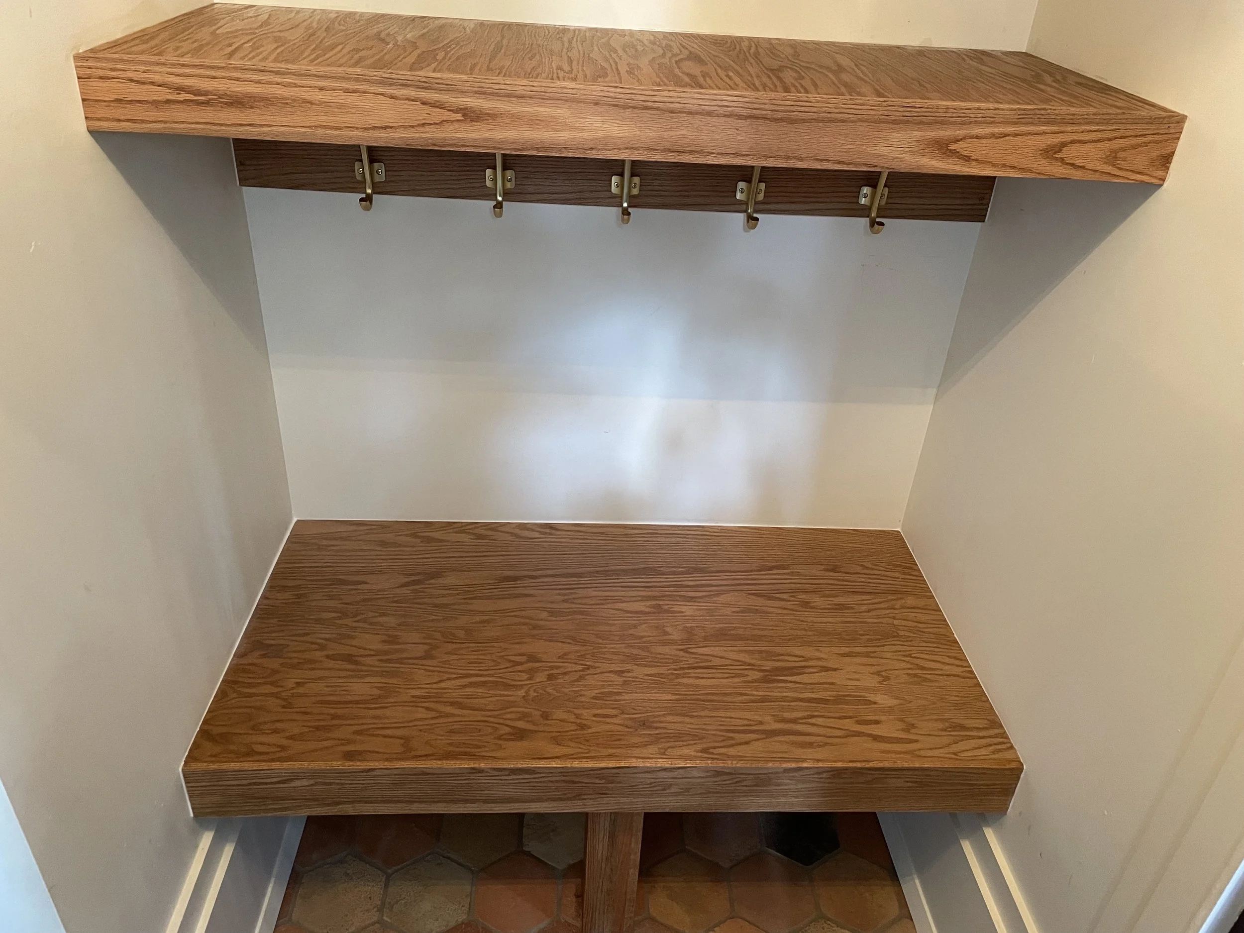 Oak wood grain and brass coat hooks in the finished entryway storage nook.