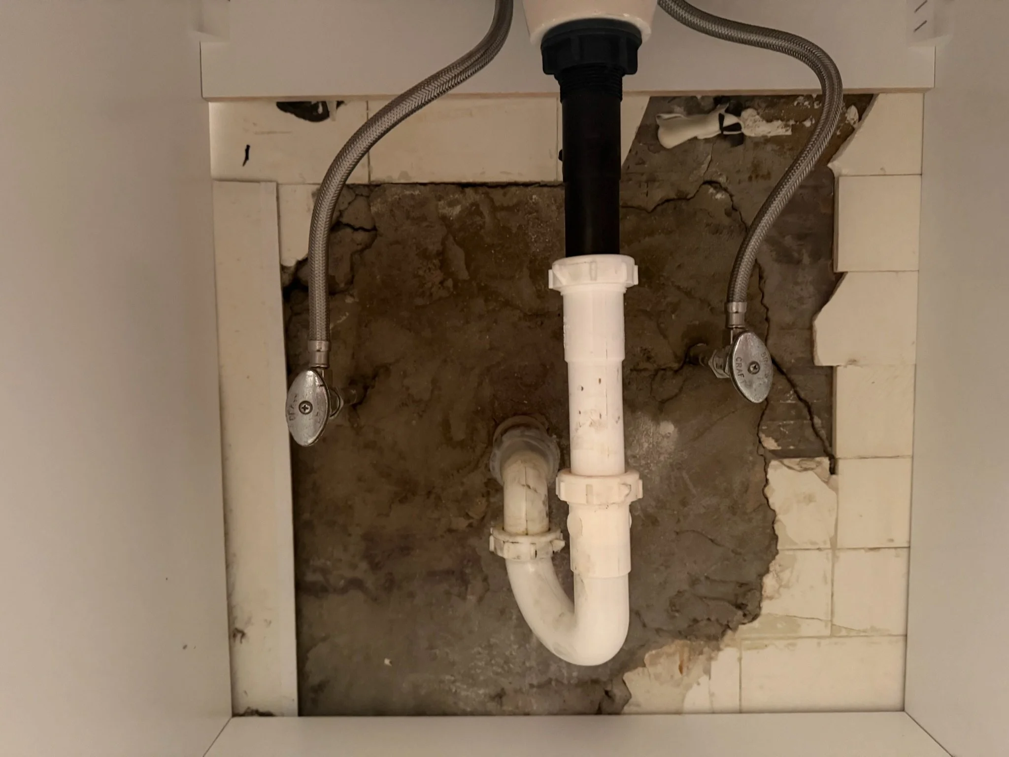 Drain and supply connections inside the vanity, with the wall surface visible behind it.