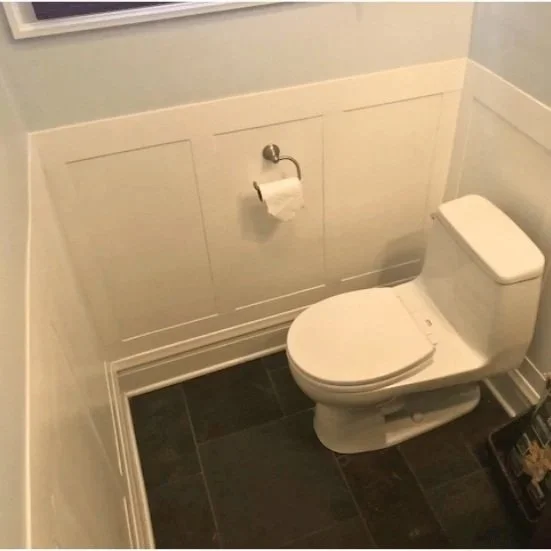 White-painted wood wainscoting with rectangular panels, chair rail and baseboard trim in a bathroom with dark slate flooring.