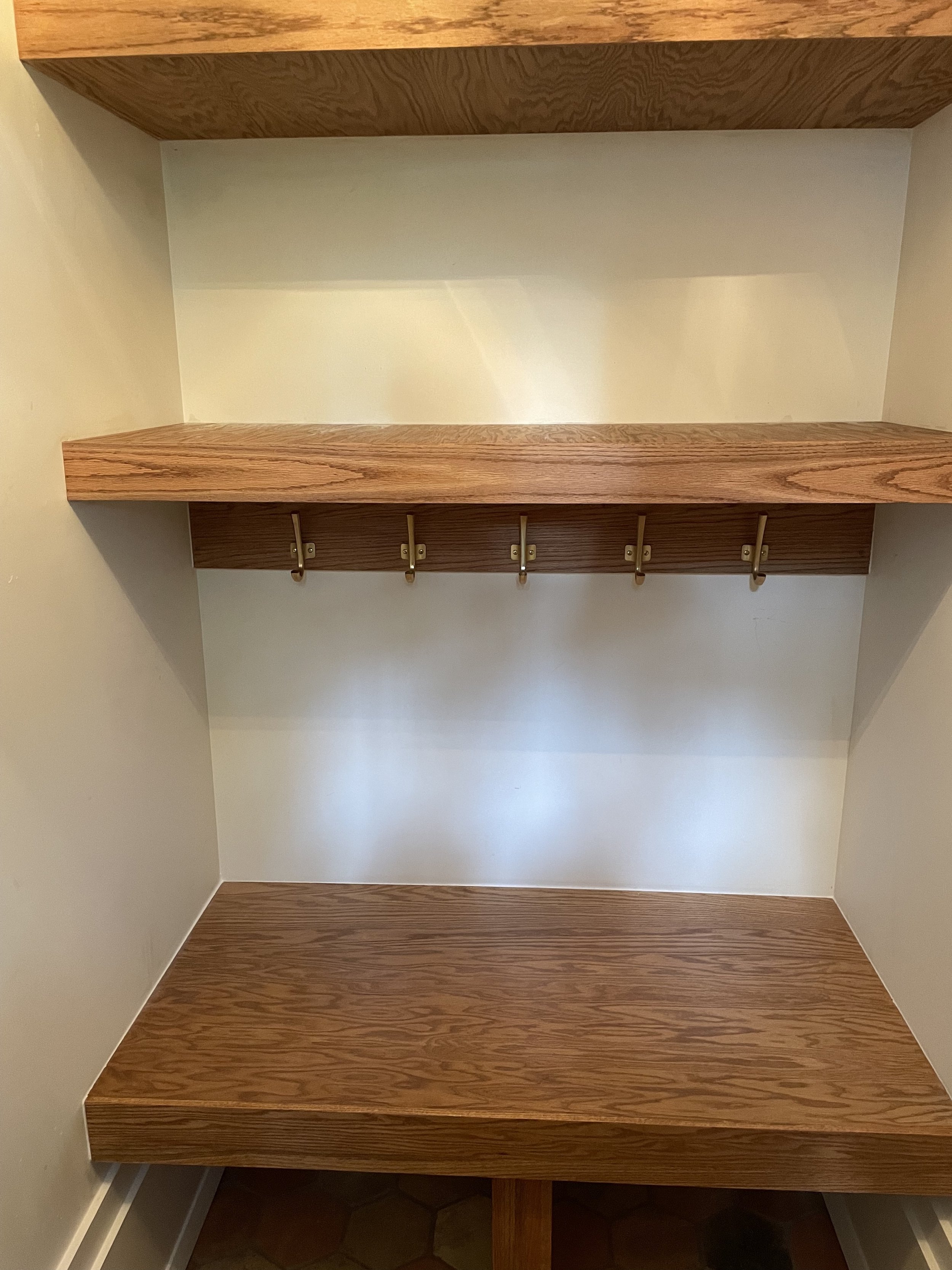 Completed oak entry bench with two floating shelves and coat hooks.