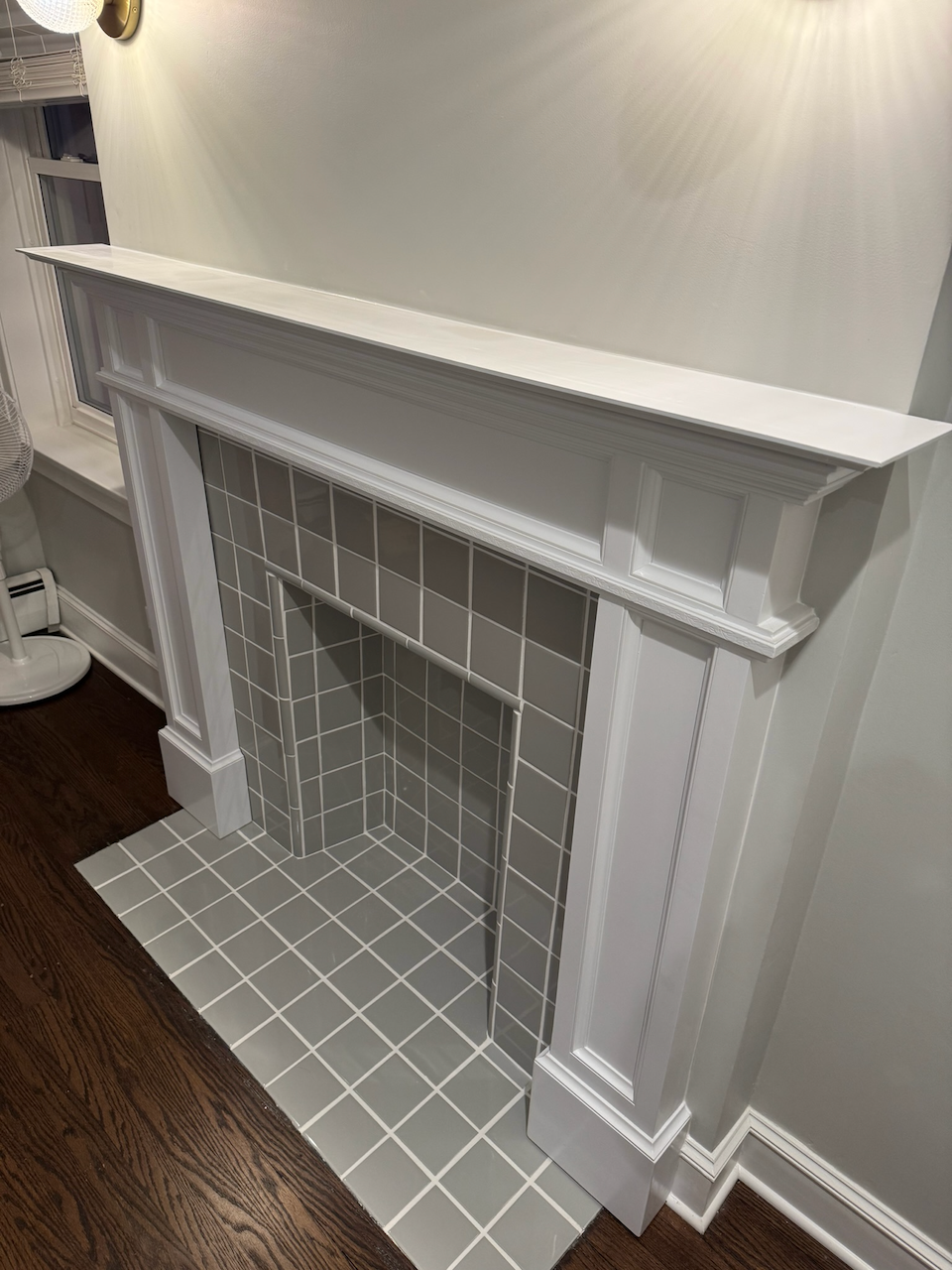 Angled view of the completed white fireplace mantel and paneled surround.