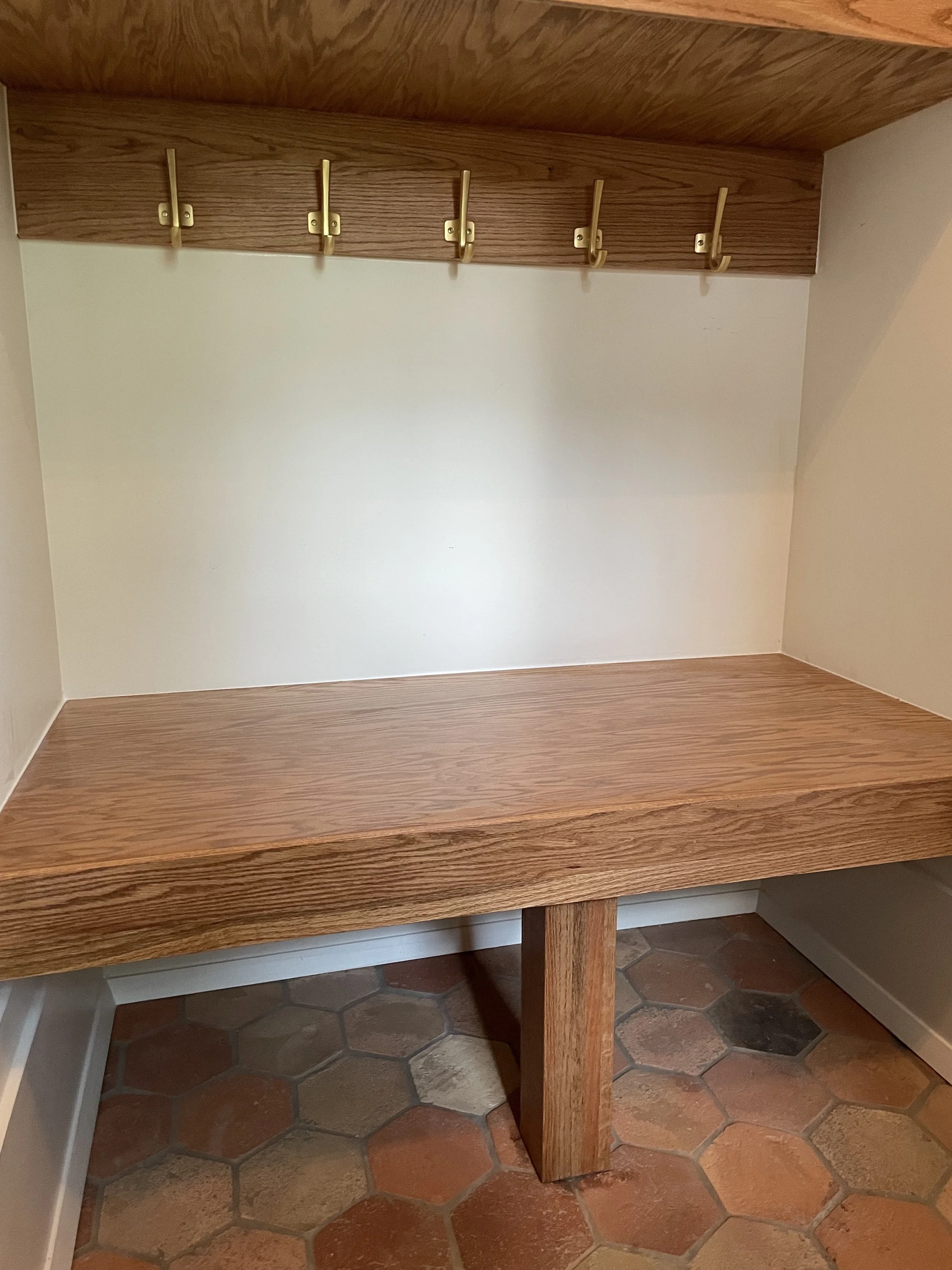 Close view of the oak bench seat, central support and brass coat hooks.