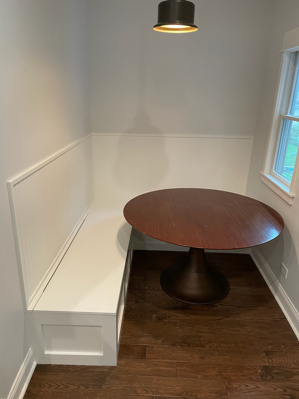 Completed L-shaped kitchen banquette with white paneled storage benches and a round dining table.