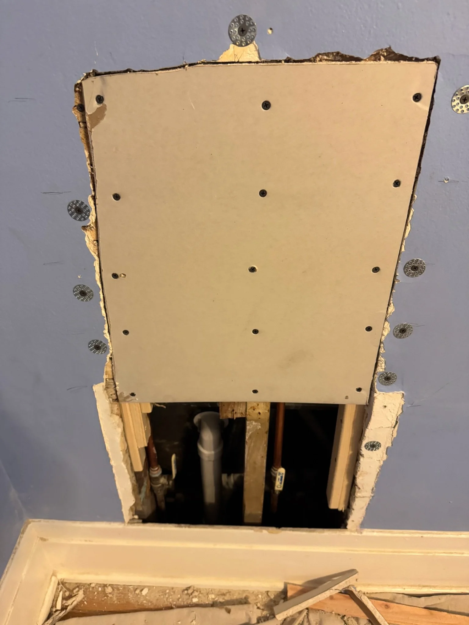 Wall repair in progress: drywall fitted around an opening, with pipes visible below.