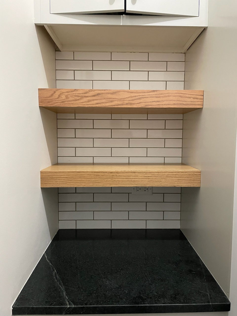 Two thick natural wood floating shelves in a tiled kitchen niche.