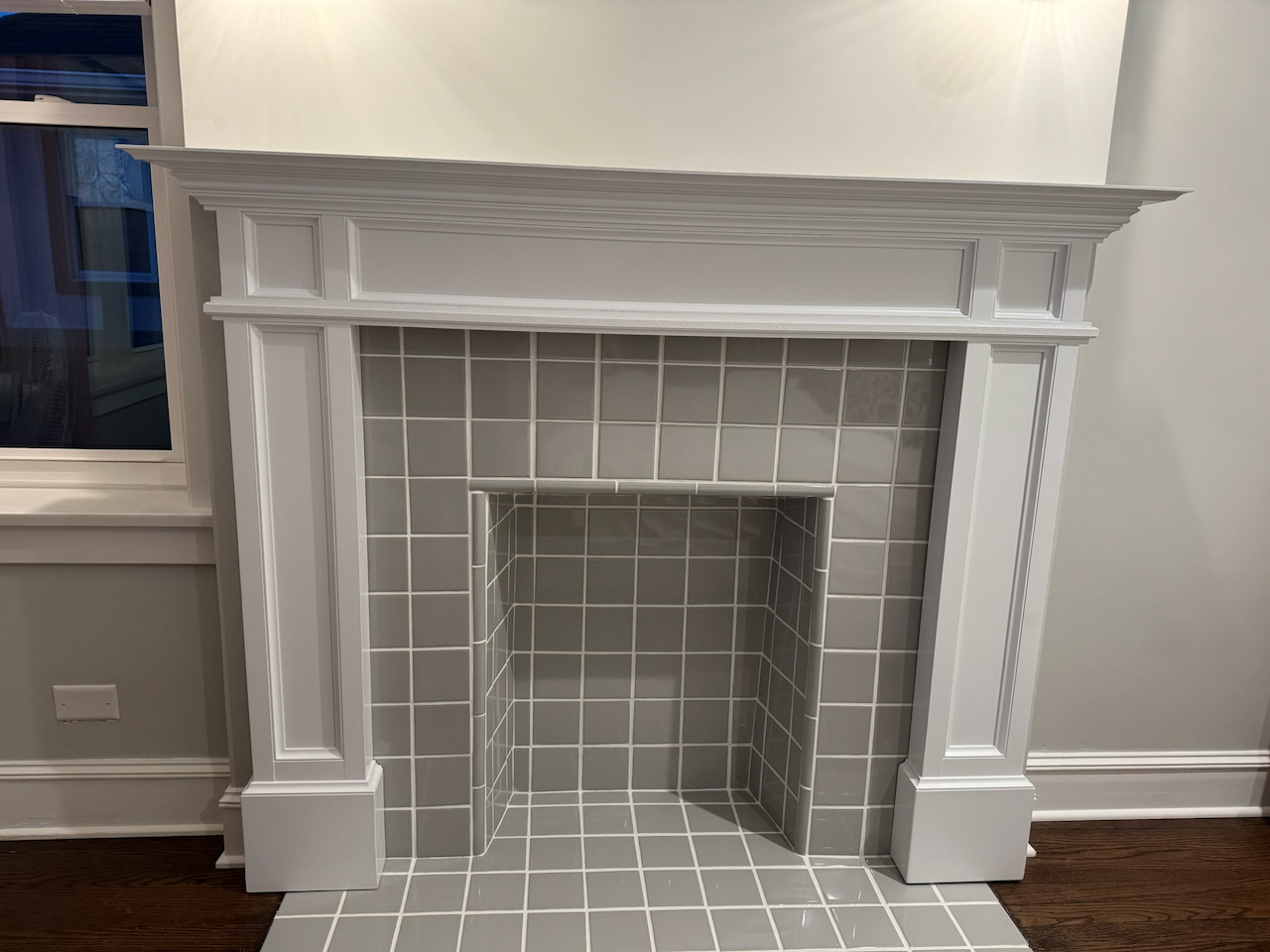 Finished white custom fireplace mantel and surround with decorative trim and gray tile.