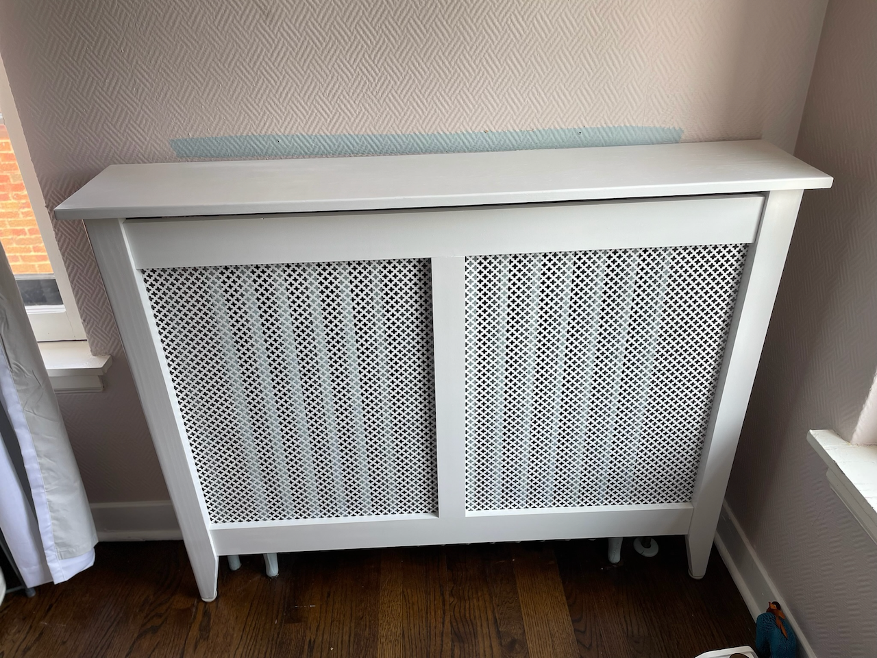 Completed white radiator cover with decorative metal grille panels and a broad top shelf.