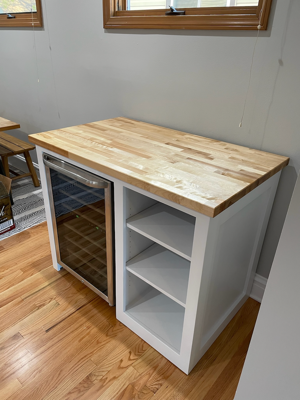 Finished custom wine bar with butcher-block countertop, beverage cooler opening and open bottle storage shelves.
