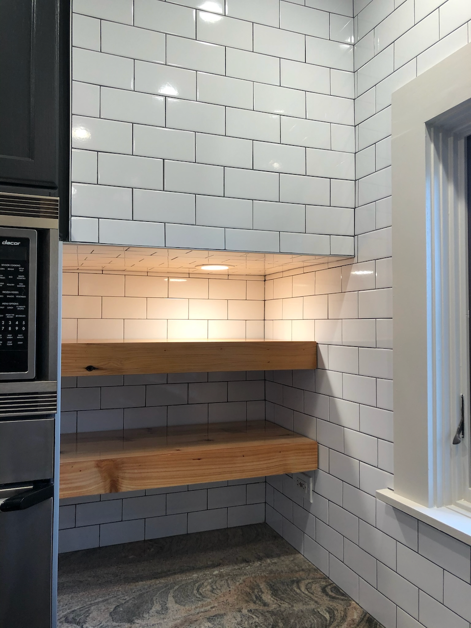 Natural wood shelves fitted into an illuminated tiled kitchen niche.