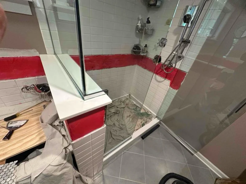 Shower tile replacement in progress around the glass enclosure
