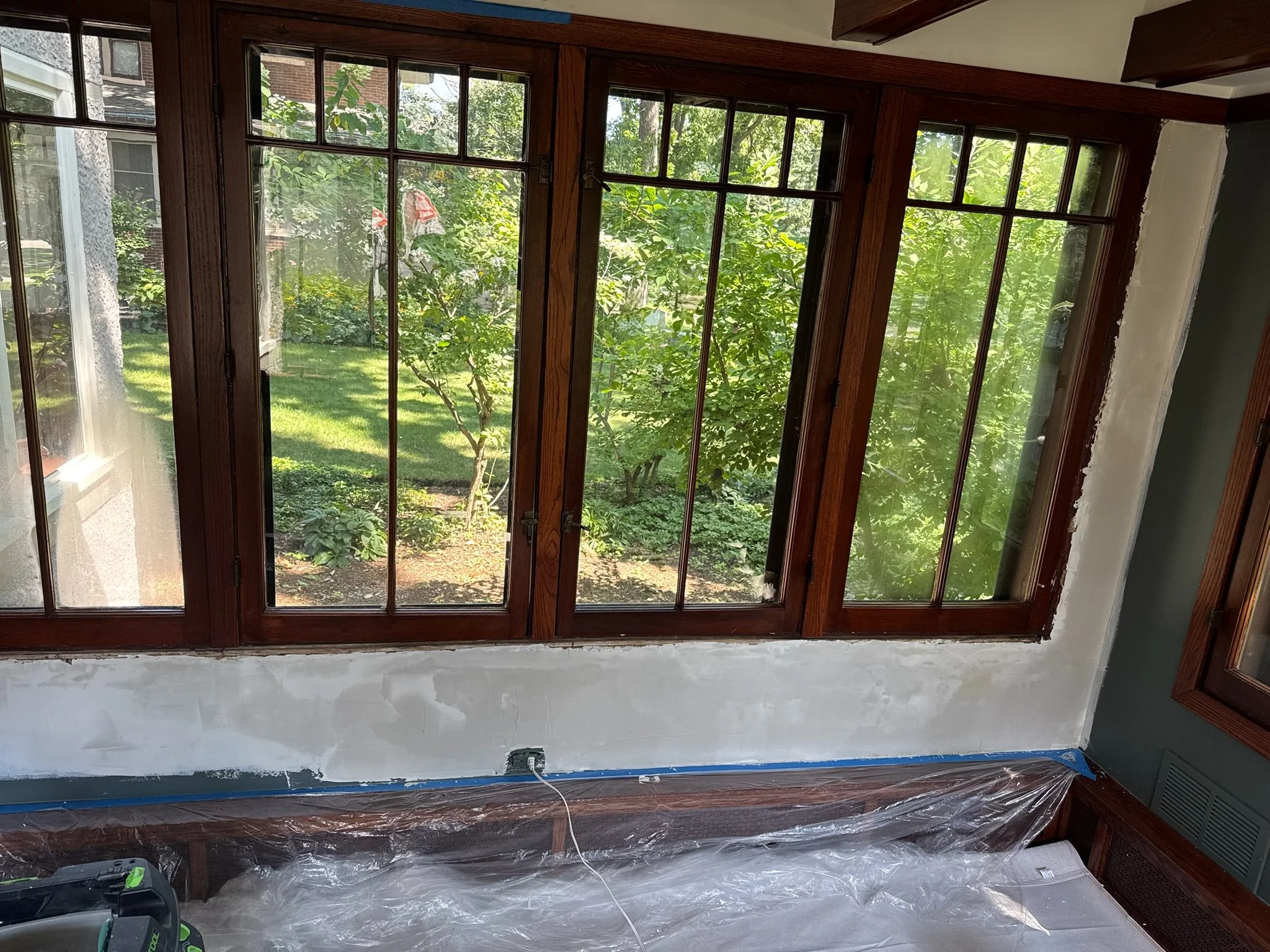 Wall repair in progress beneath and around wood-framed windows.