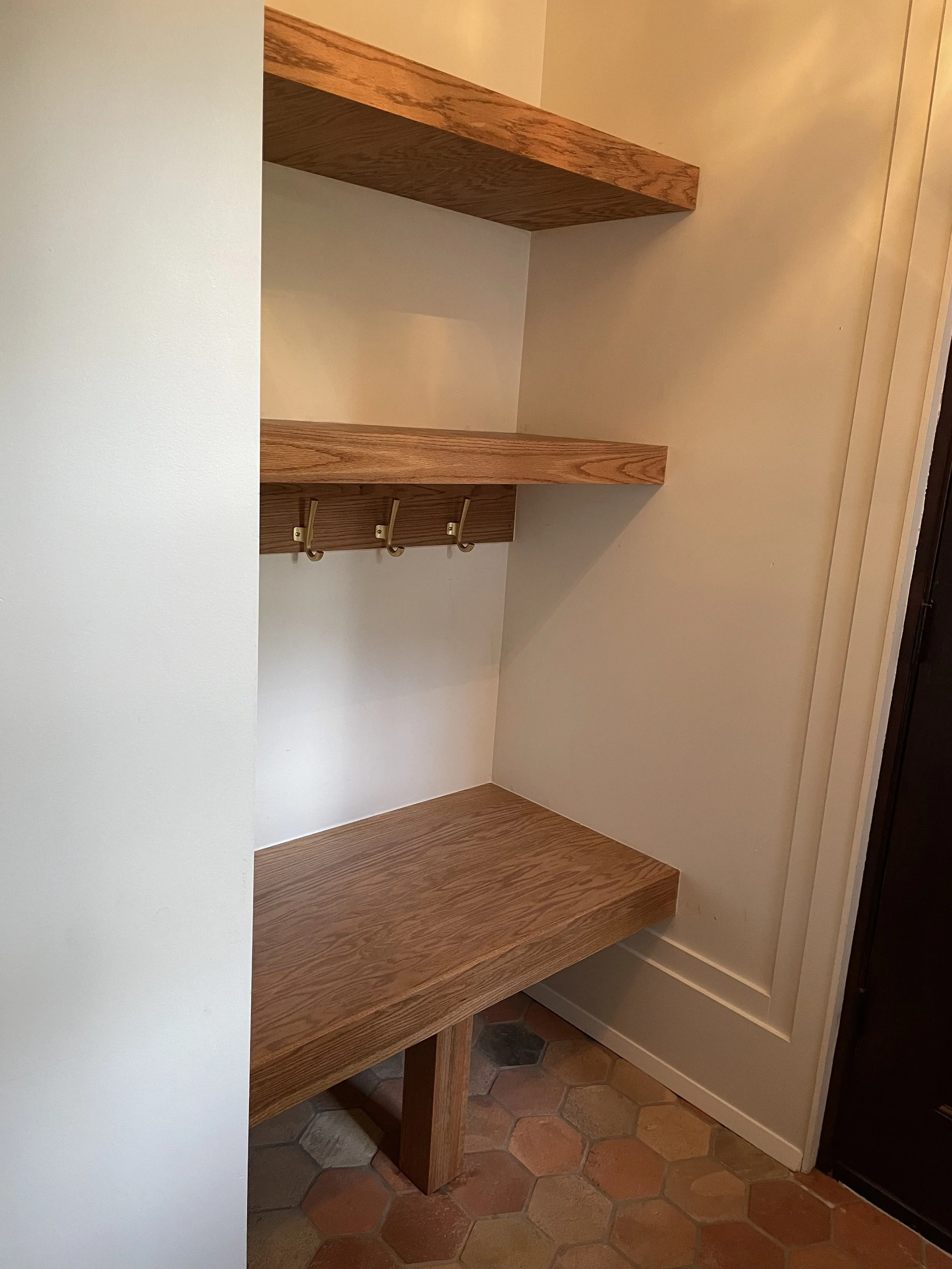 Side view of the custom oak entry bench, floating shelves and brass coat hooks.