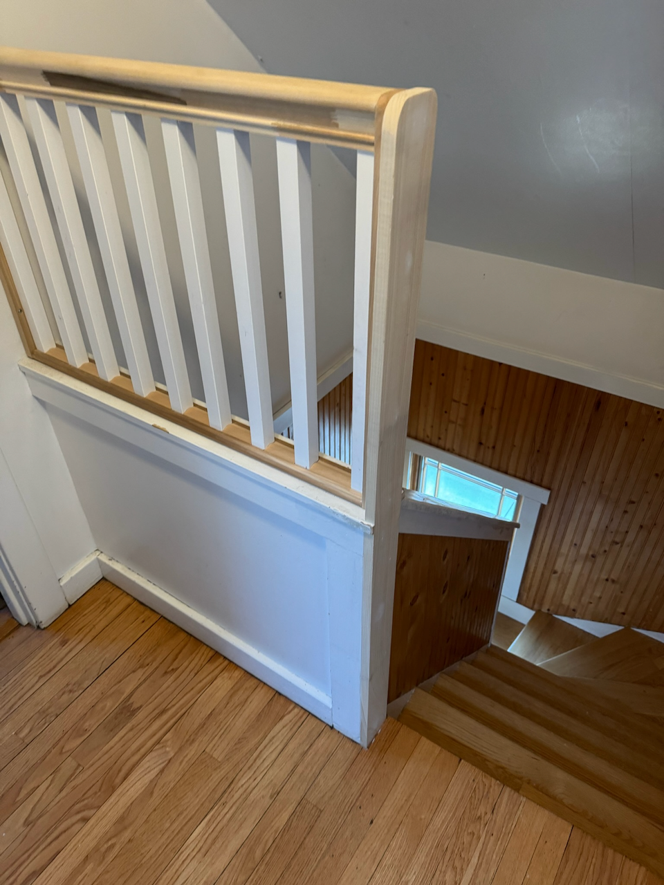 Stair landing railing with white balusters and natural wood handrail.