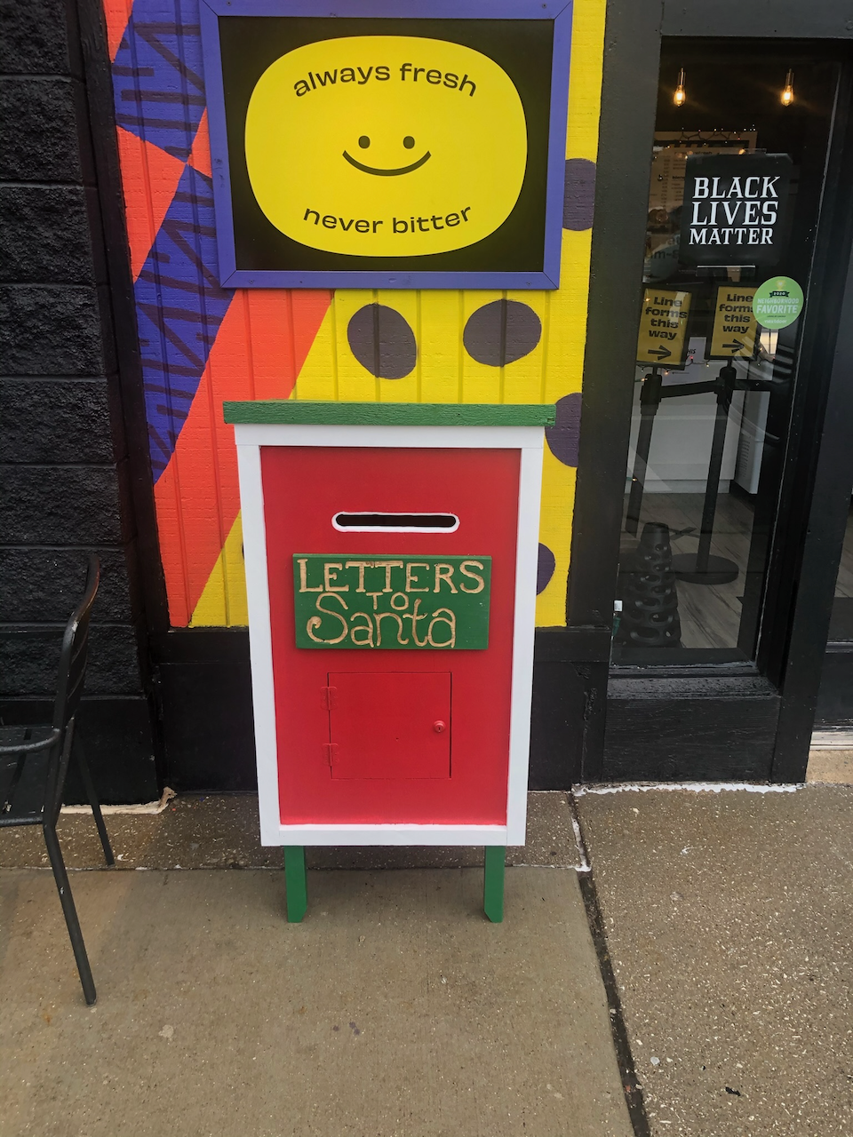 Red Santa mailbox with white border and green trim outside the storefront.