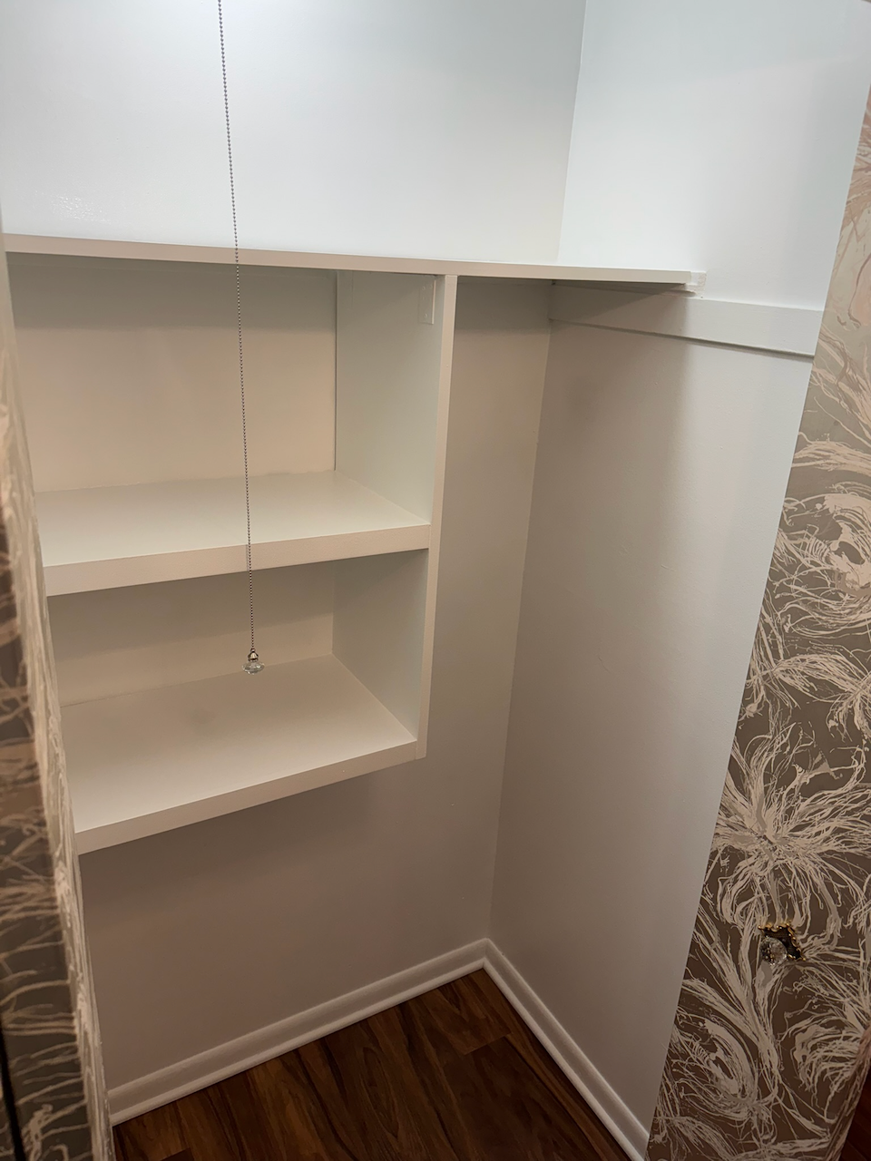 Built-in storage shelves and hanging space beside the wallpapered wall.