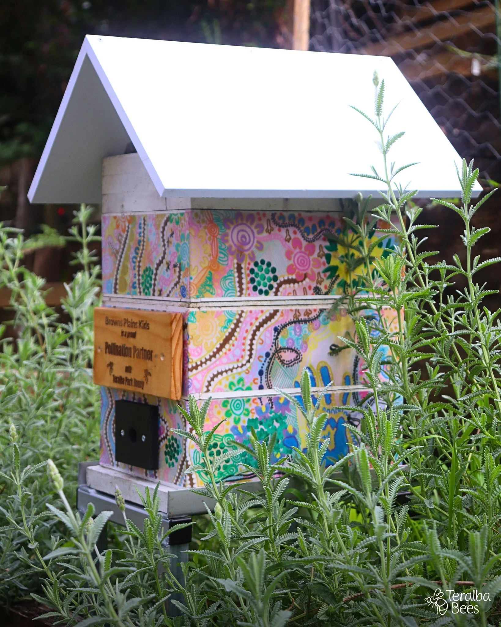 Building with a stone facade and sign that reads "Bring back the Wildhood for Kids". In front, there is a colorful mailbox with a floral design and a small wooden roof, and outdoor seating with benches.