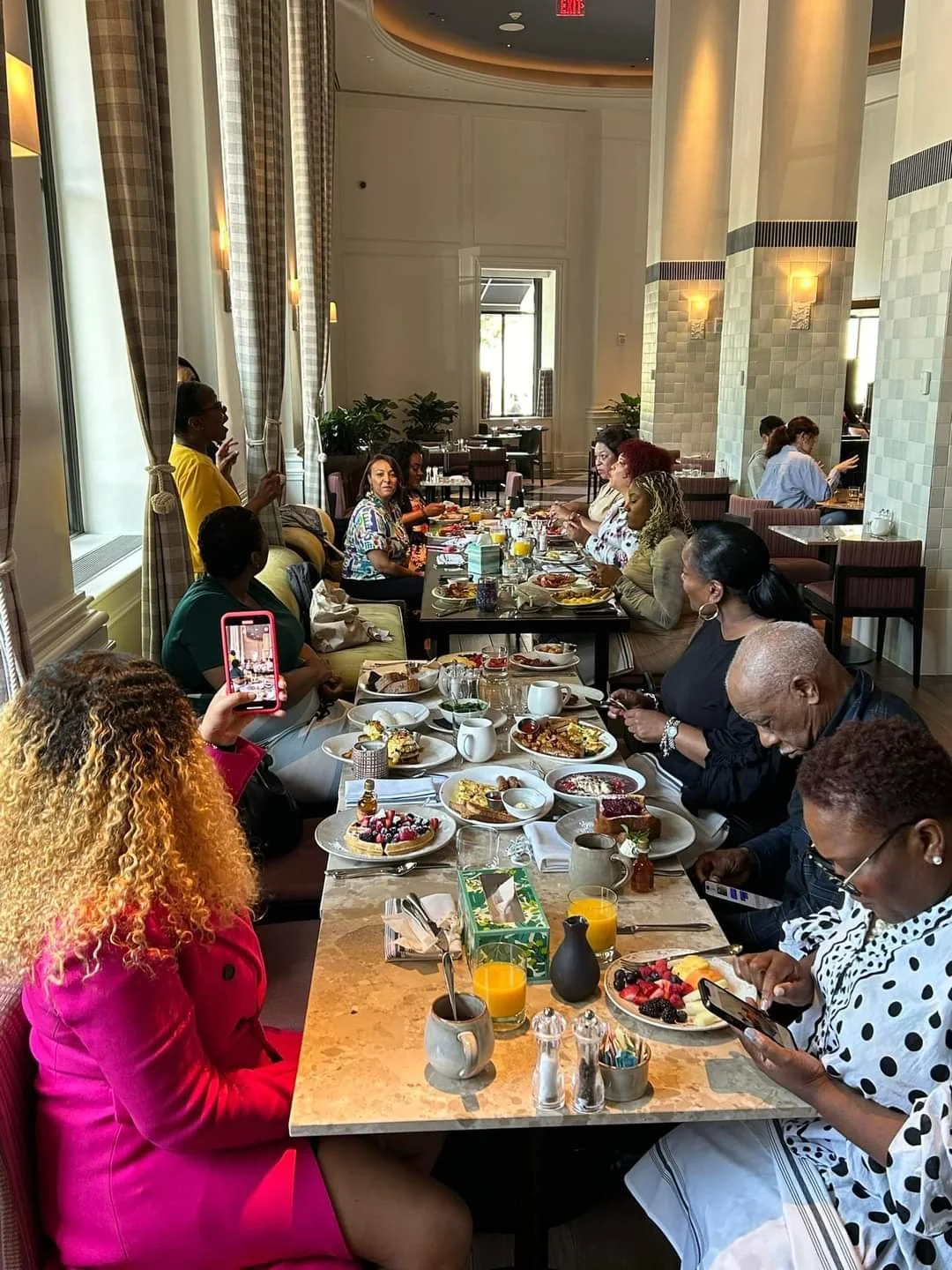 Group of people dining at a restaurant table with plates of food and drinks, including fruit and breakfast items.