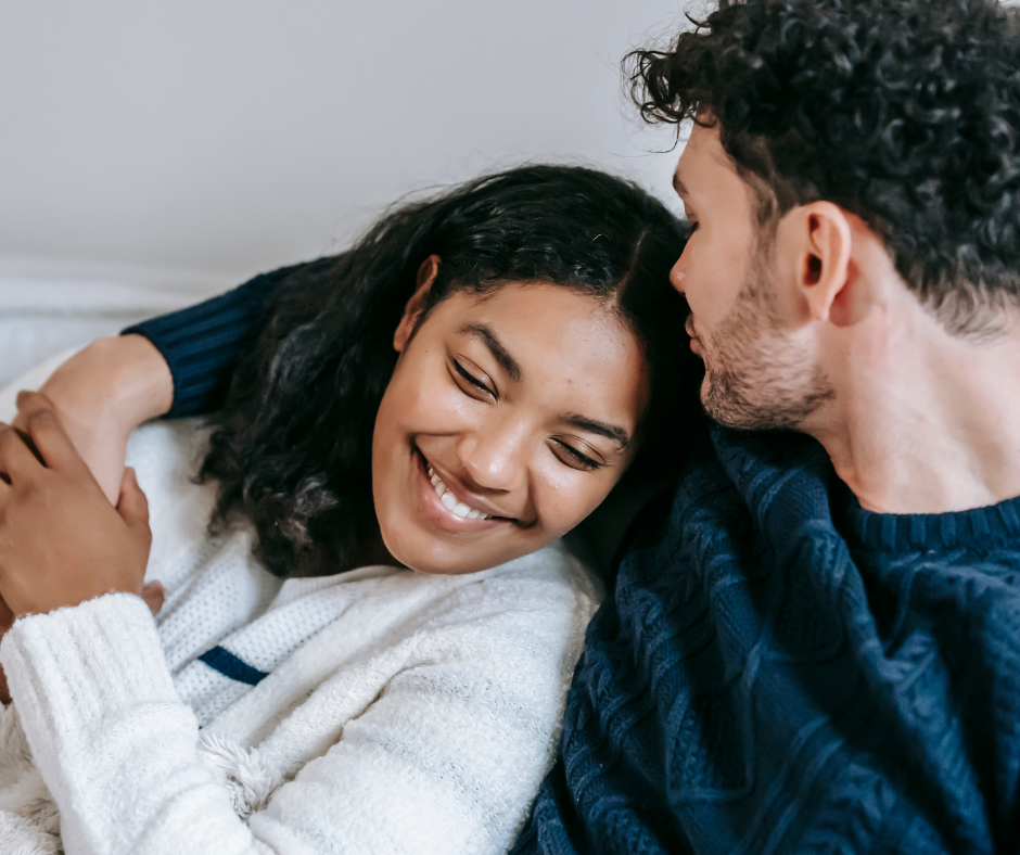 Smiling couple cuddling in bed, feeling emotionally safe and connected