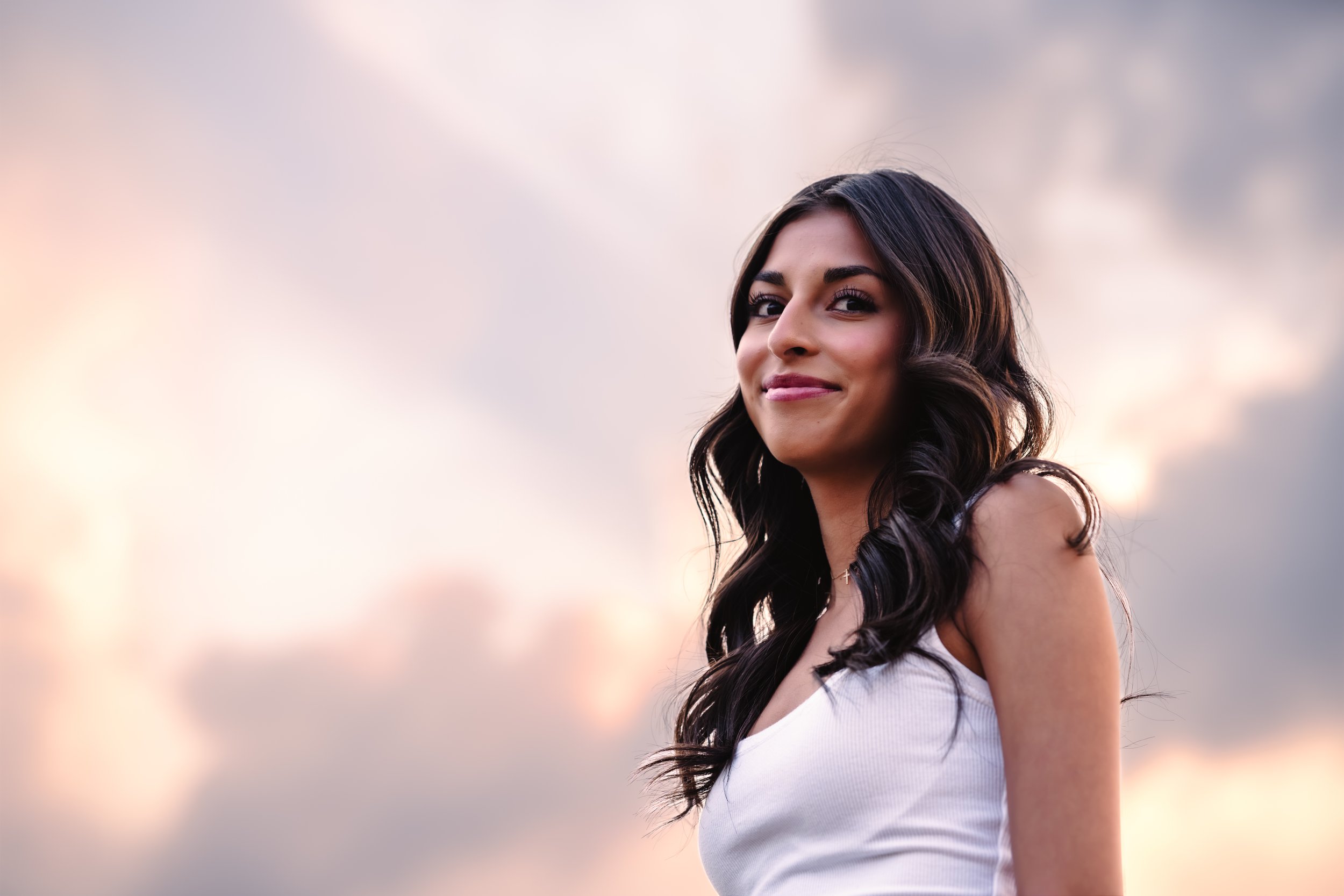 High school senior looks down at the photographer with a sunset in the background.