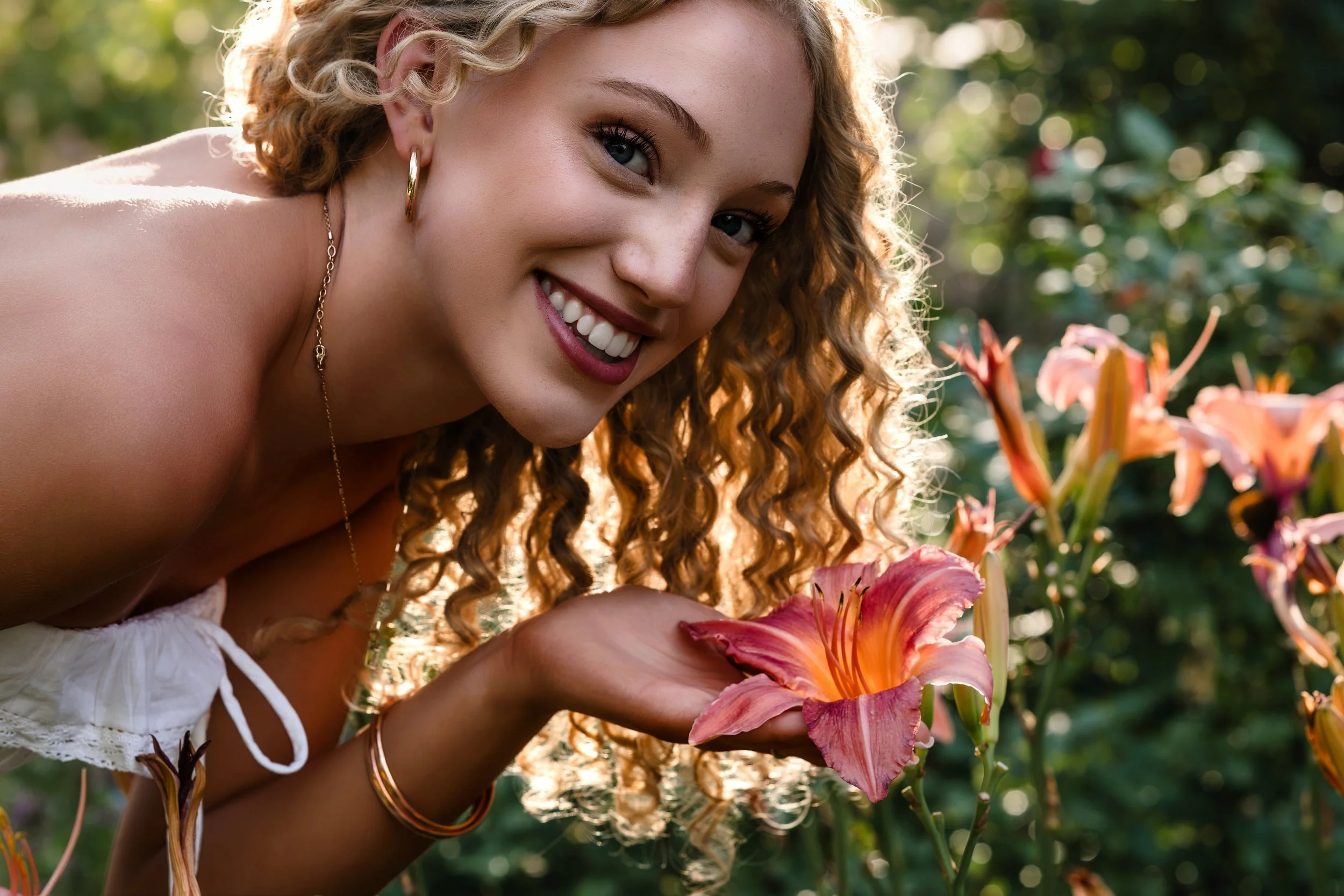 Girl with blonde curly hair smells a flower during her senior pictures at the Denver Botanic Gardens