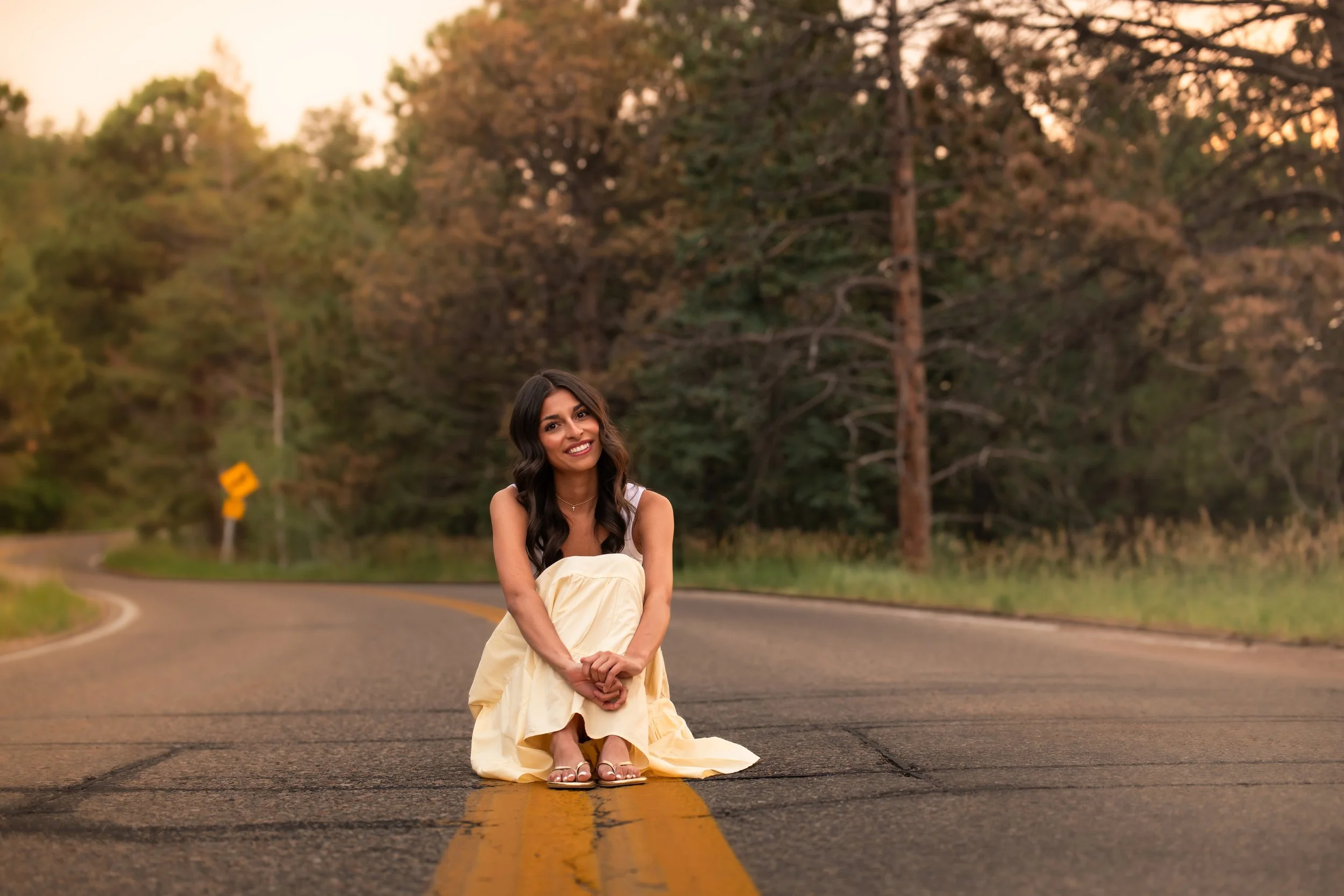 High school girl in a white top and a yellow skirt cradles her legs as she sits in the middle of a street.