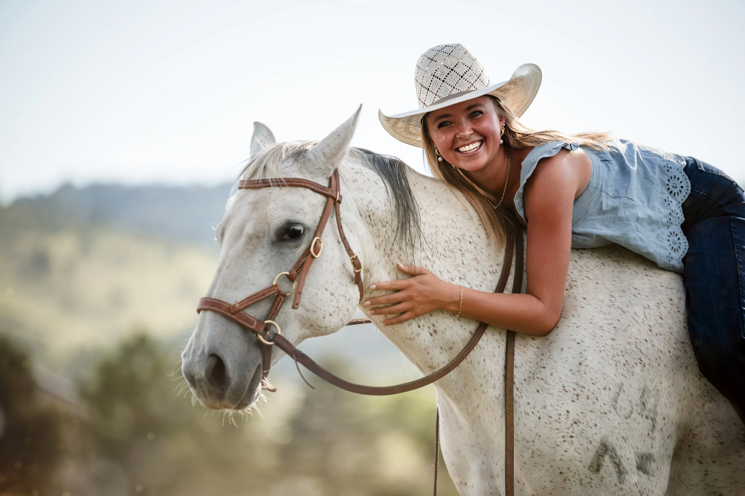 A blonde girl with a big smile leans over on a white horse.