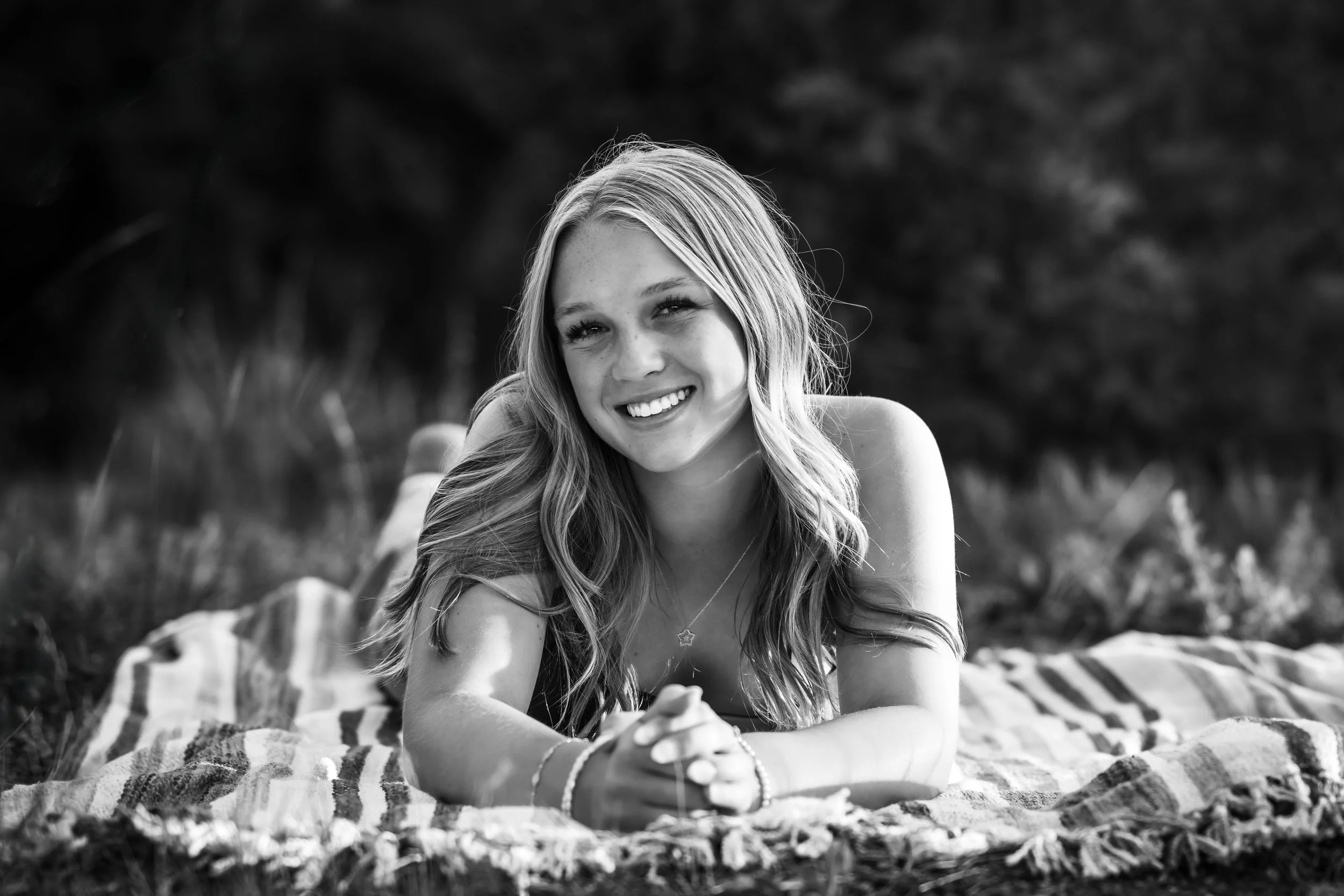 Blonde girl lays on a striped picnic blanket in a field.