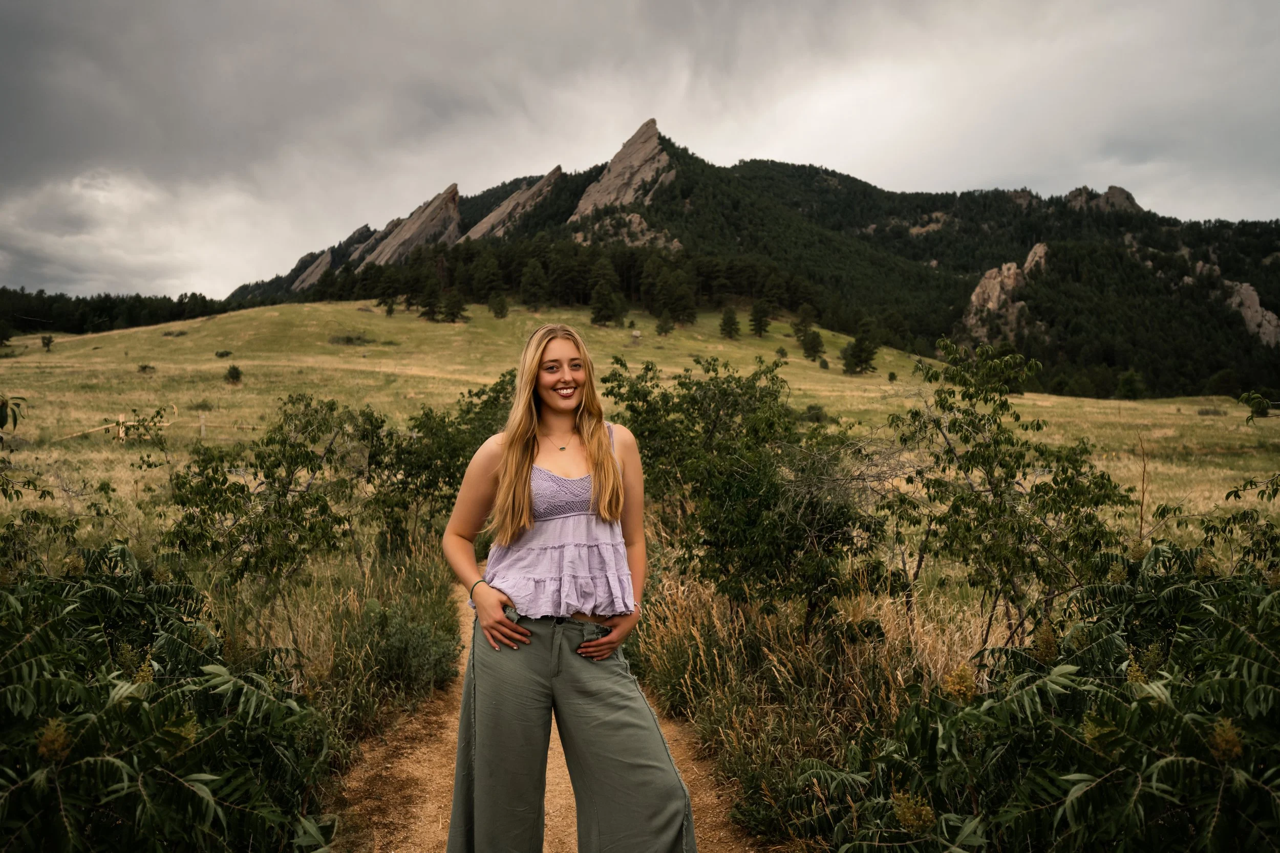A girl in a purple tank top and army green pants stands in front of Chautauqua park for her senior pictures in Boulder.