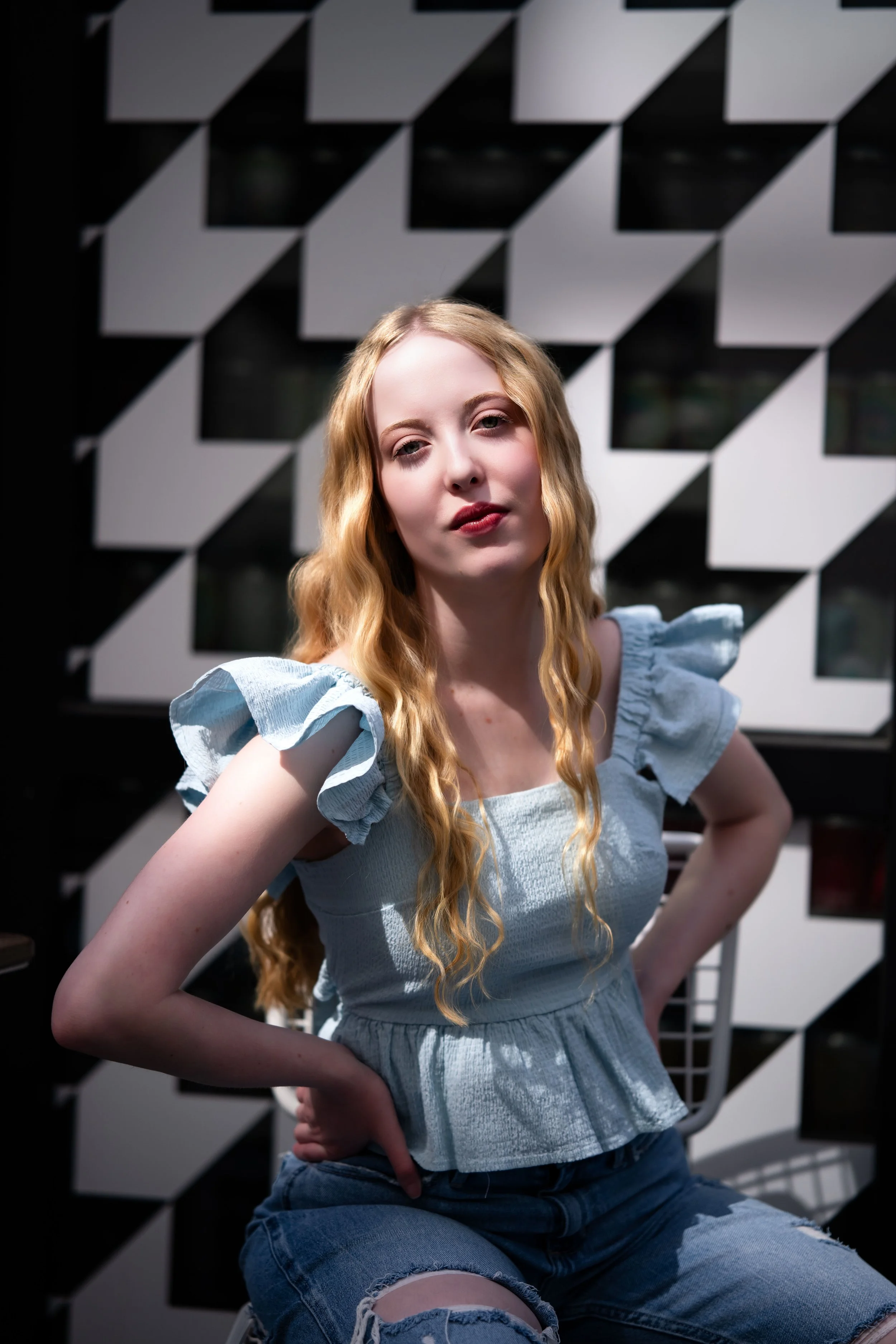 A girl with long blonde hair stands in front of a checkered black and white wall at the Dairy Block in Downtown Denver for her senior pictures.