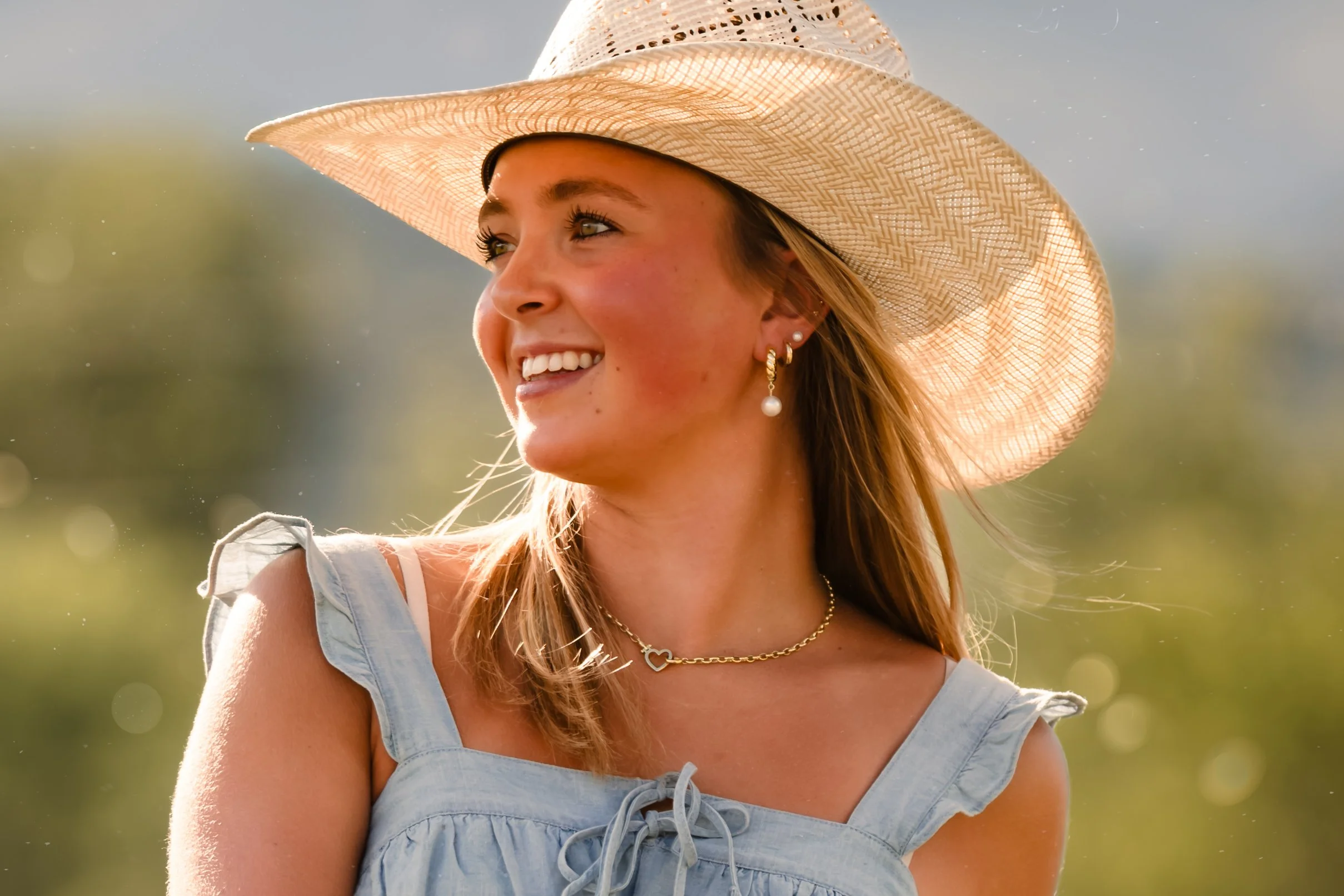 Blonde girl in straw hat has a big smile as she looks off into the distance.