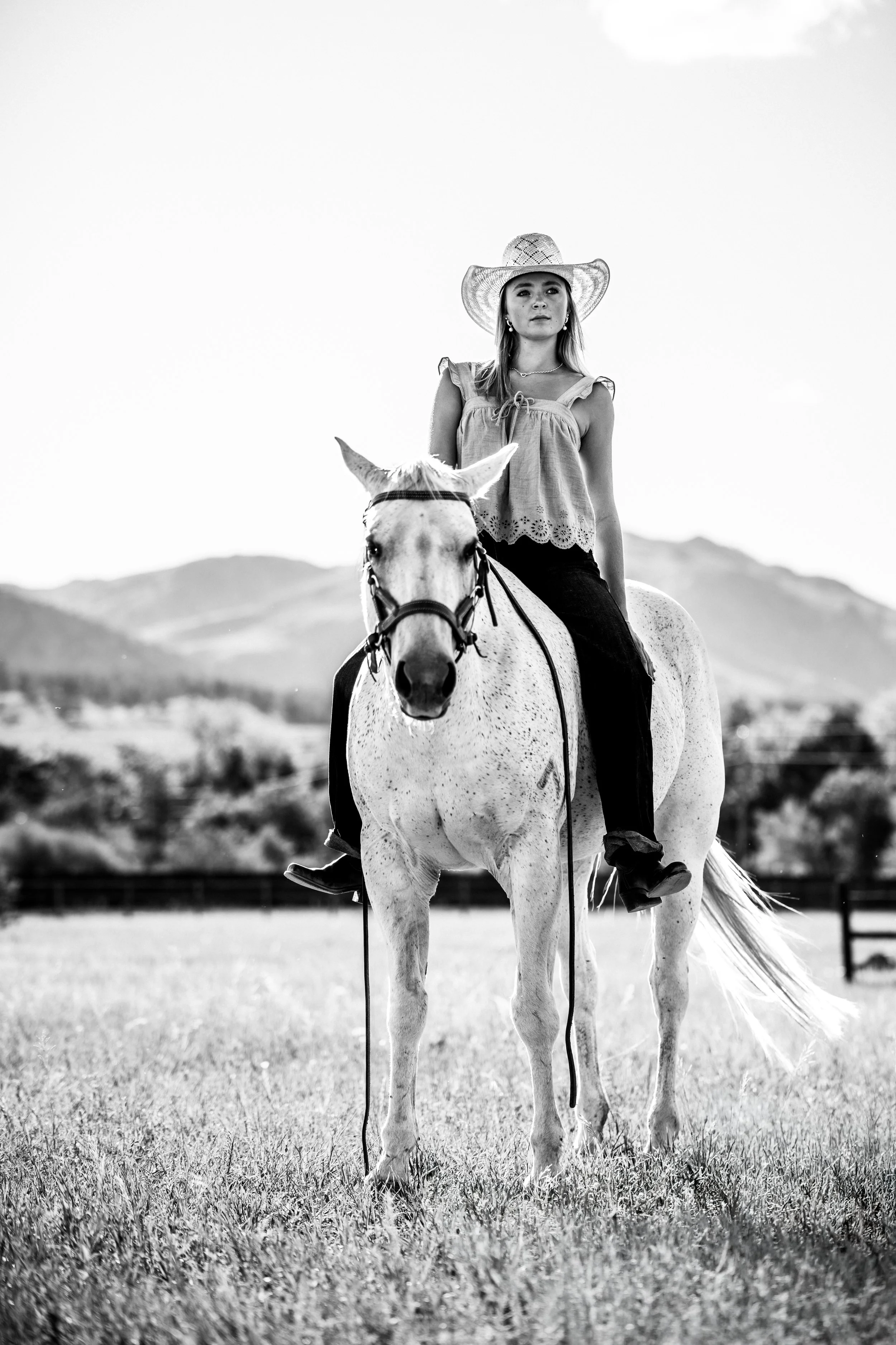 Teen girl with a straw cowboy hat rides a white horse for her senior photos in Boulder. 