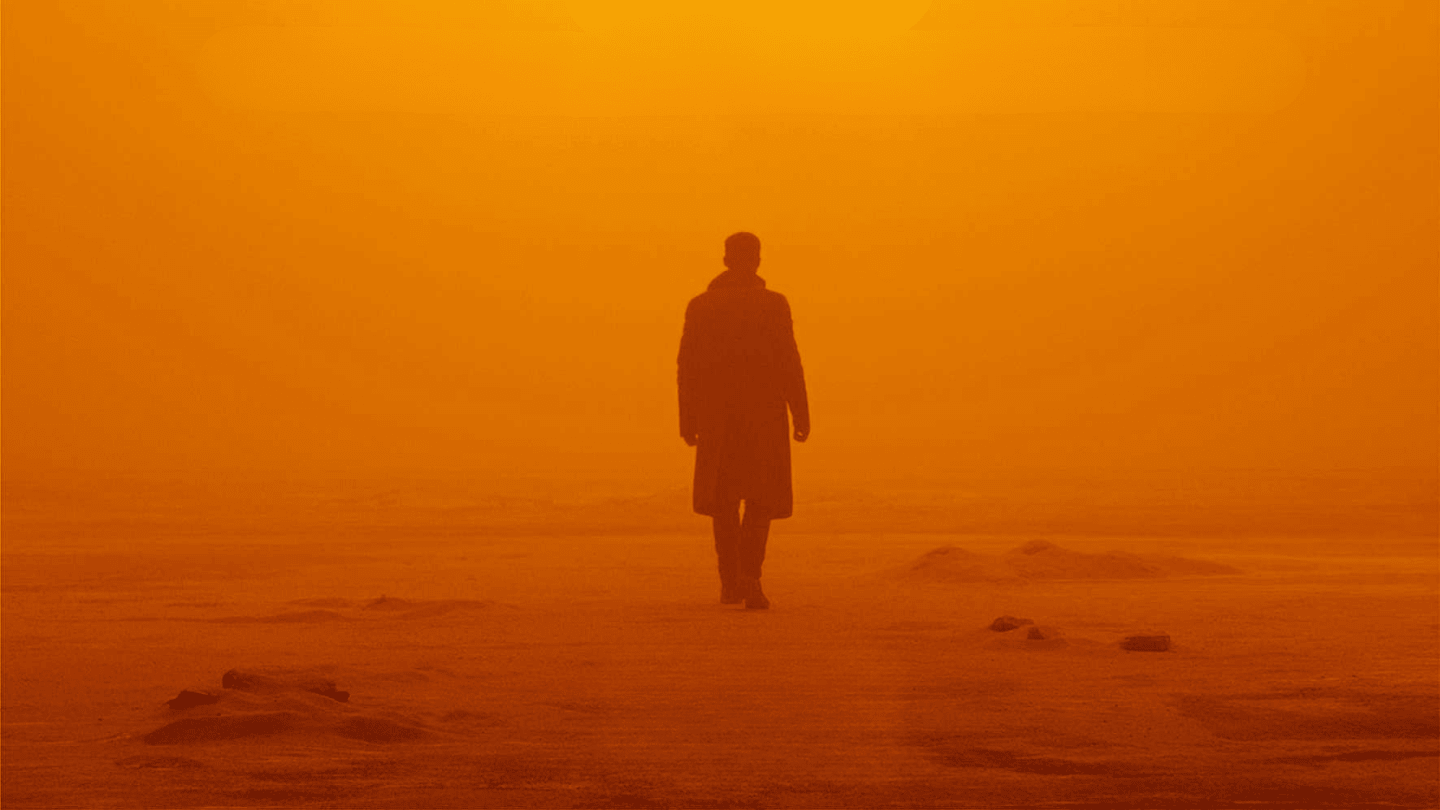 A solitary figures walks alone against an orange sky