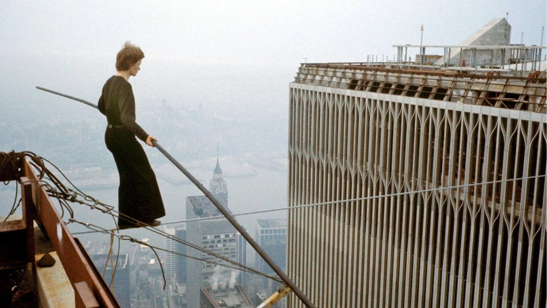 A man on a tightrope walking between tall buildings high in the New York skyline
