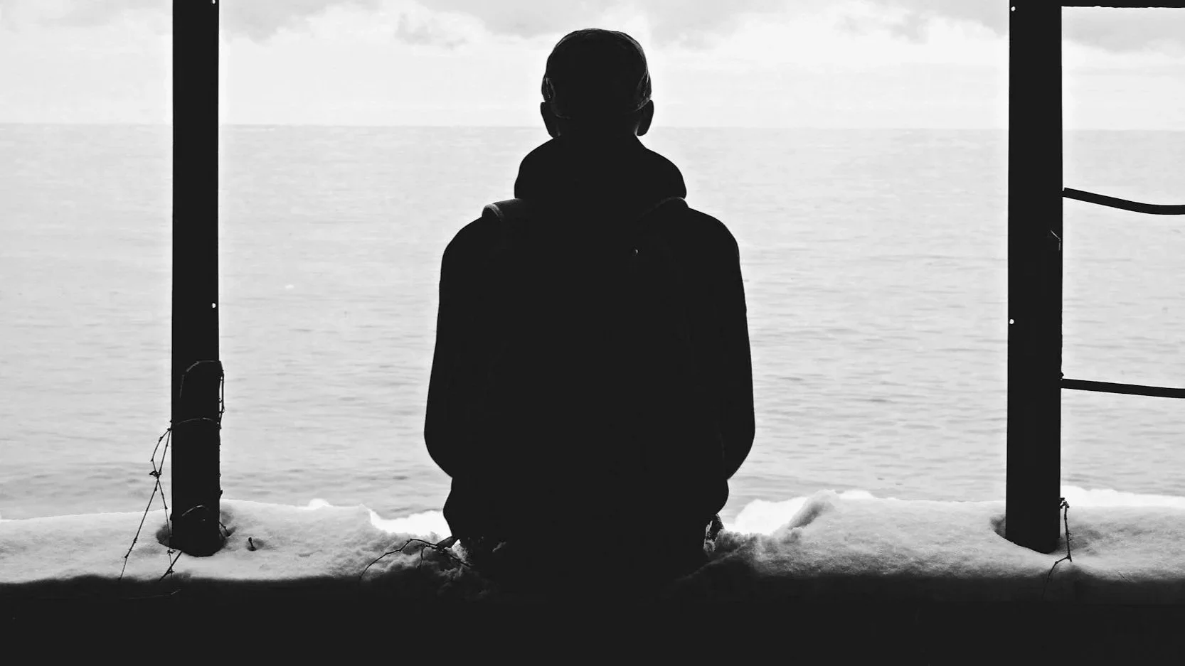 A man sits isolated staring out to sea, alone